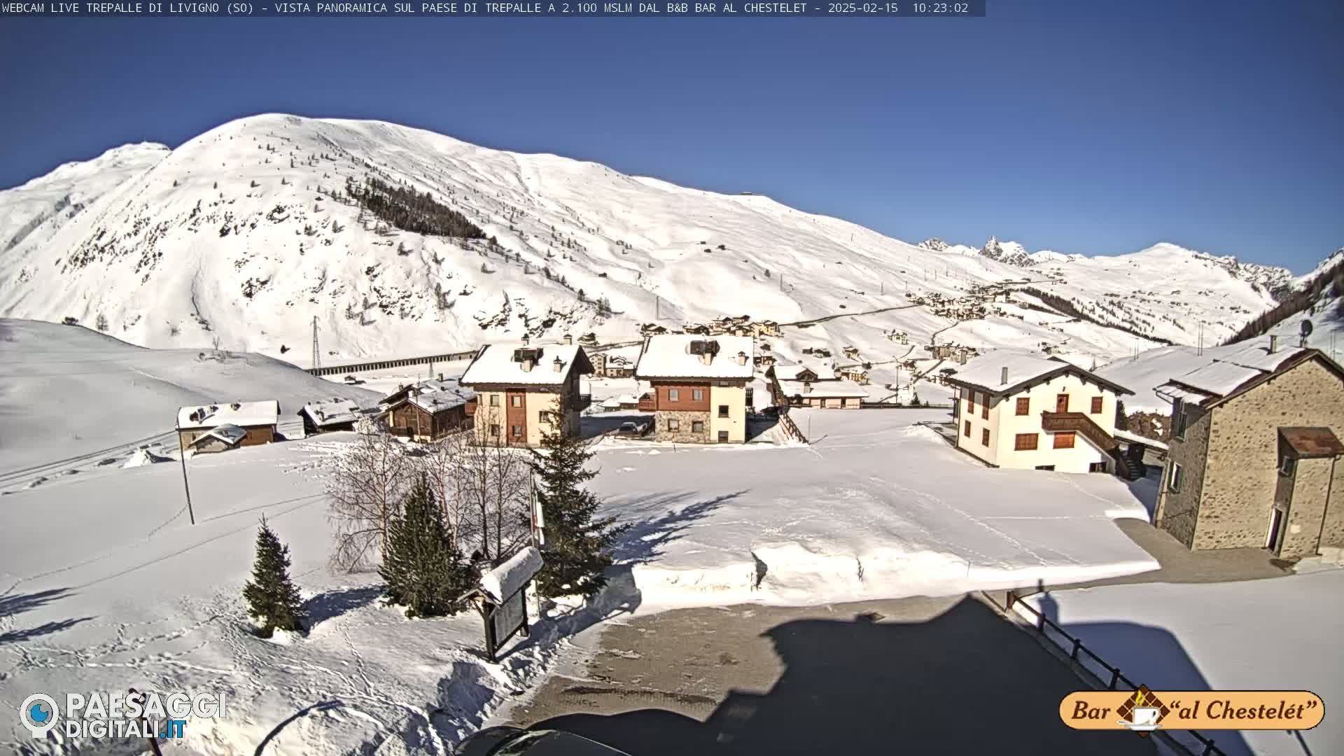 A snow-covered village nestled in a valley beneath sunlit, snow-dusted mountains.