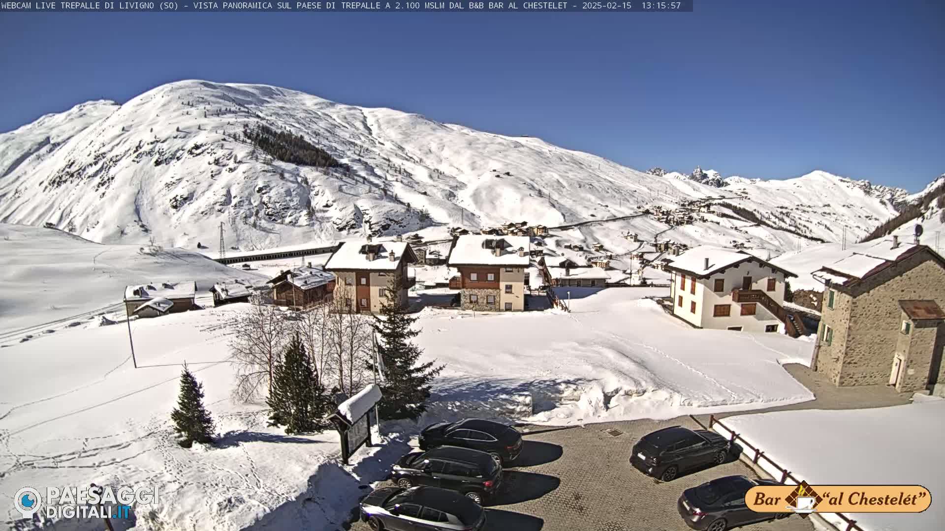 A snow-covered village nestled in a valley surrounded by snow-capped mountains under a bright, sunny sky.