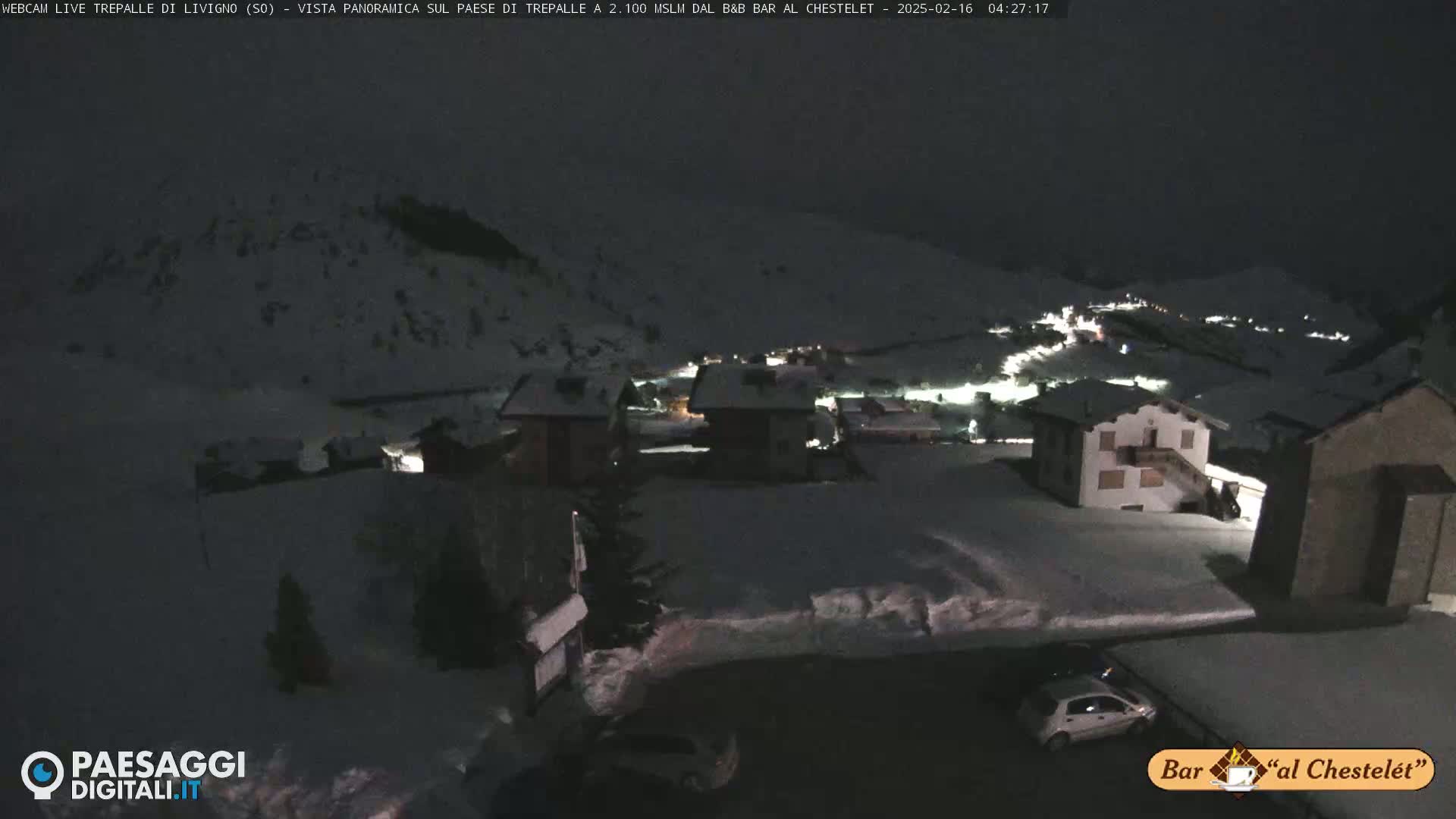 A snow-covered village is visible at night, illuminated by scattered lights, under a dark sky.