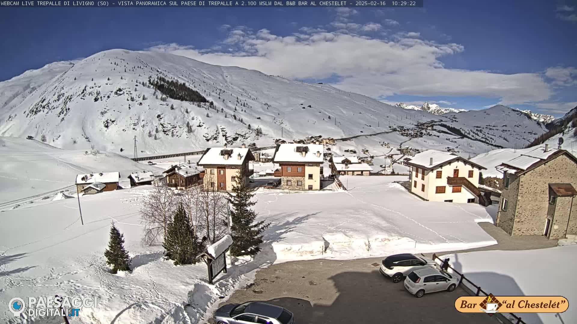 A snow-covered village nestled in a mountainous region under a partly cloudy sky.