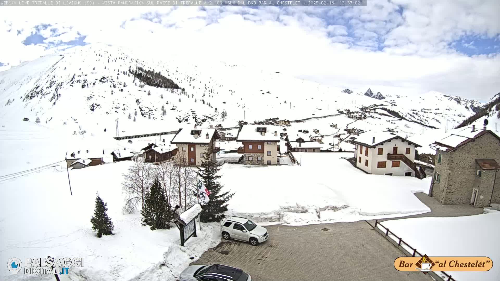 A snow-covered village nestled in a mountainous region under a partly cloudy sky.