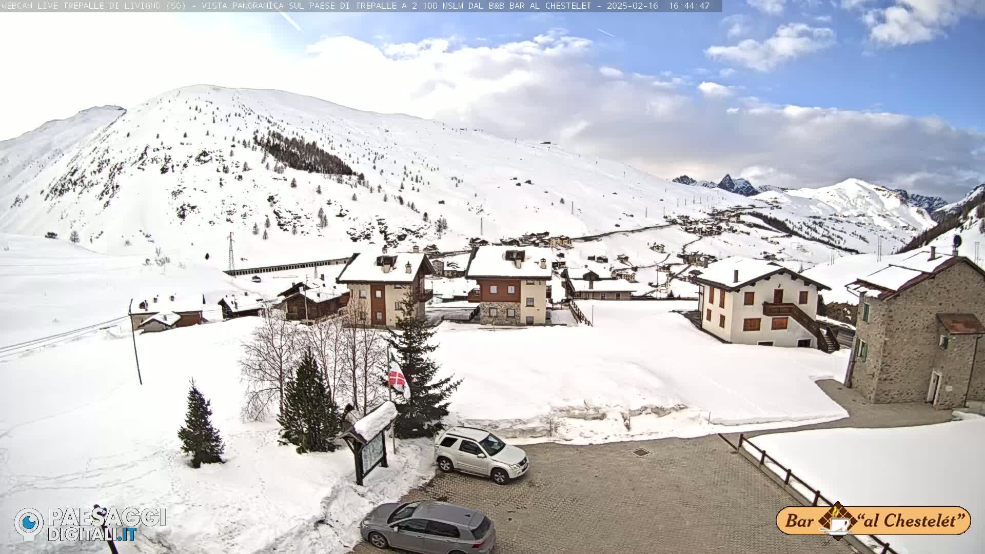 A snow-covered village nestled in a mountainous valley under a partly cloudy sky.