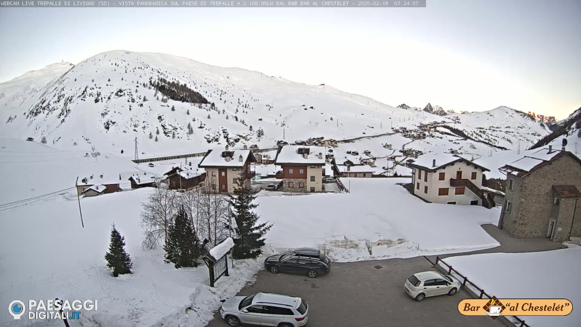 A snow-covered village nestled in a valley between snow-capped mountains under a clear, twilight sky.