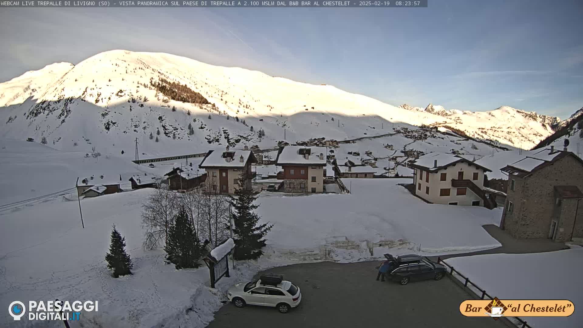 A snow-covered mountain village is nestled in a valley under a clear, sunny sky.