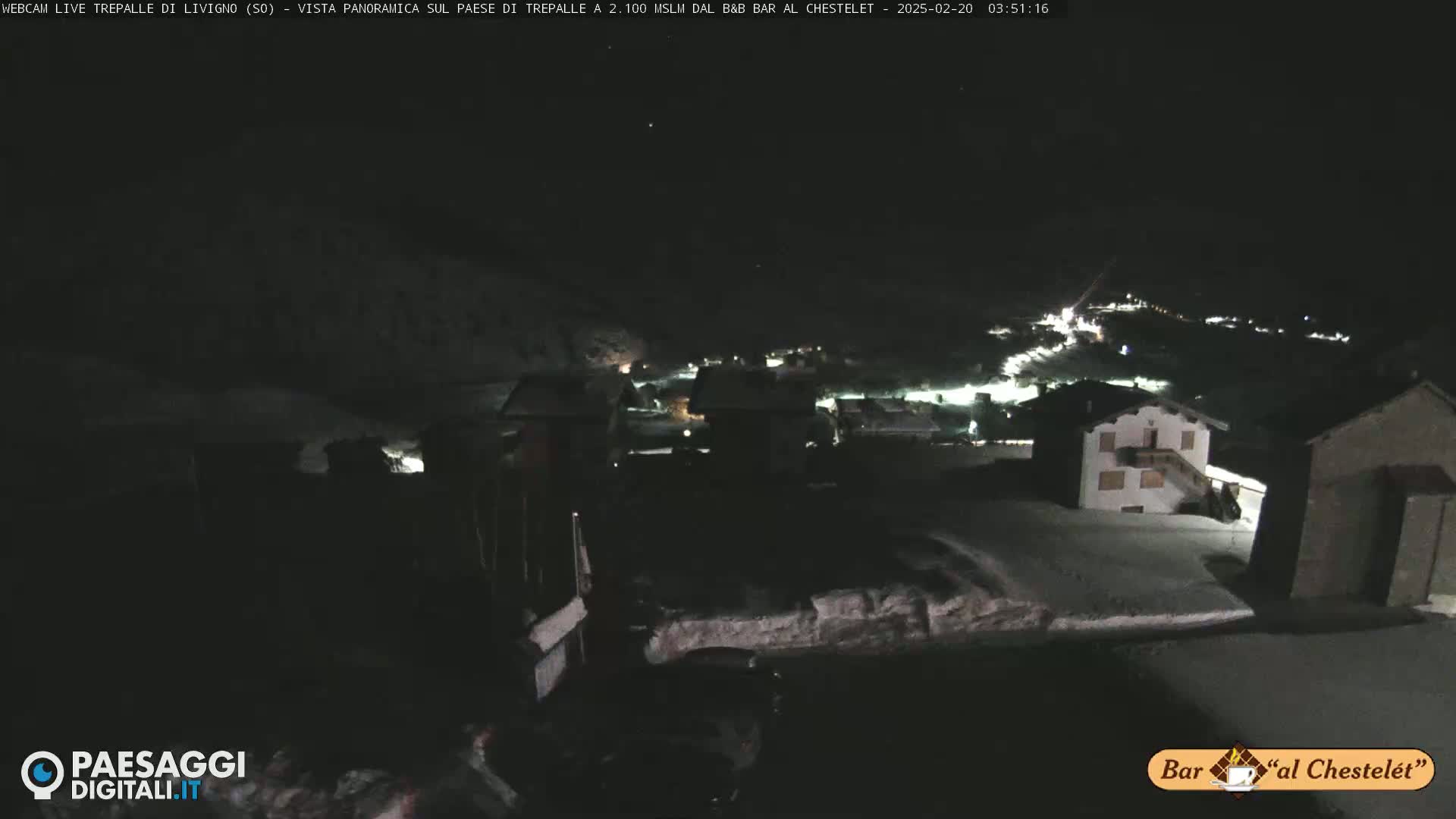 A nighttime, snow-covered village is seen from a high vantage point under a dark sky.