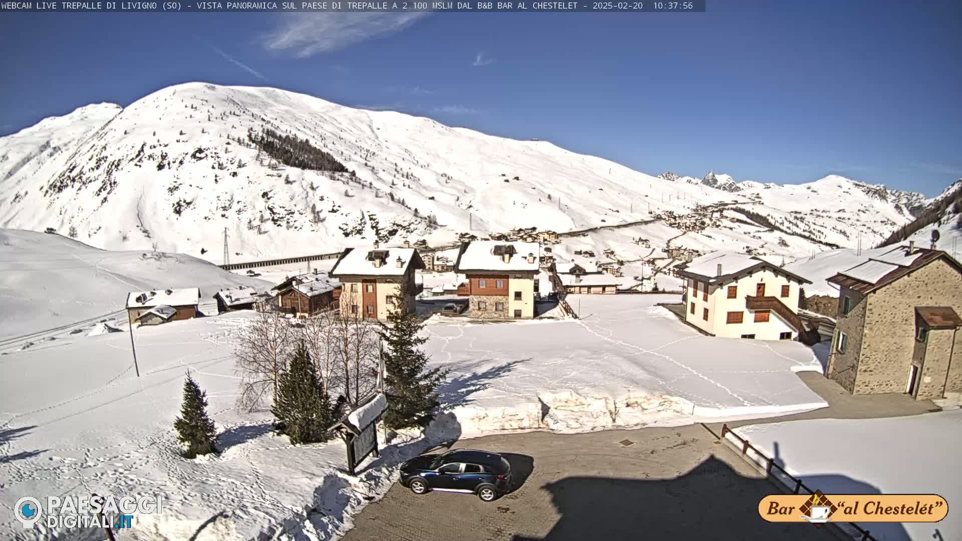 A snow-covered village nestled in a valley beneath a sunny, snow-capped mountain.
