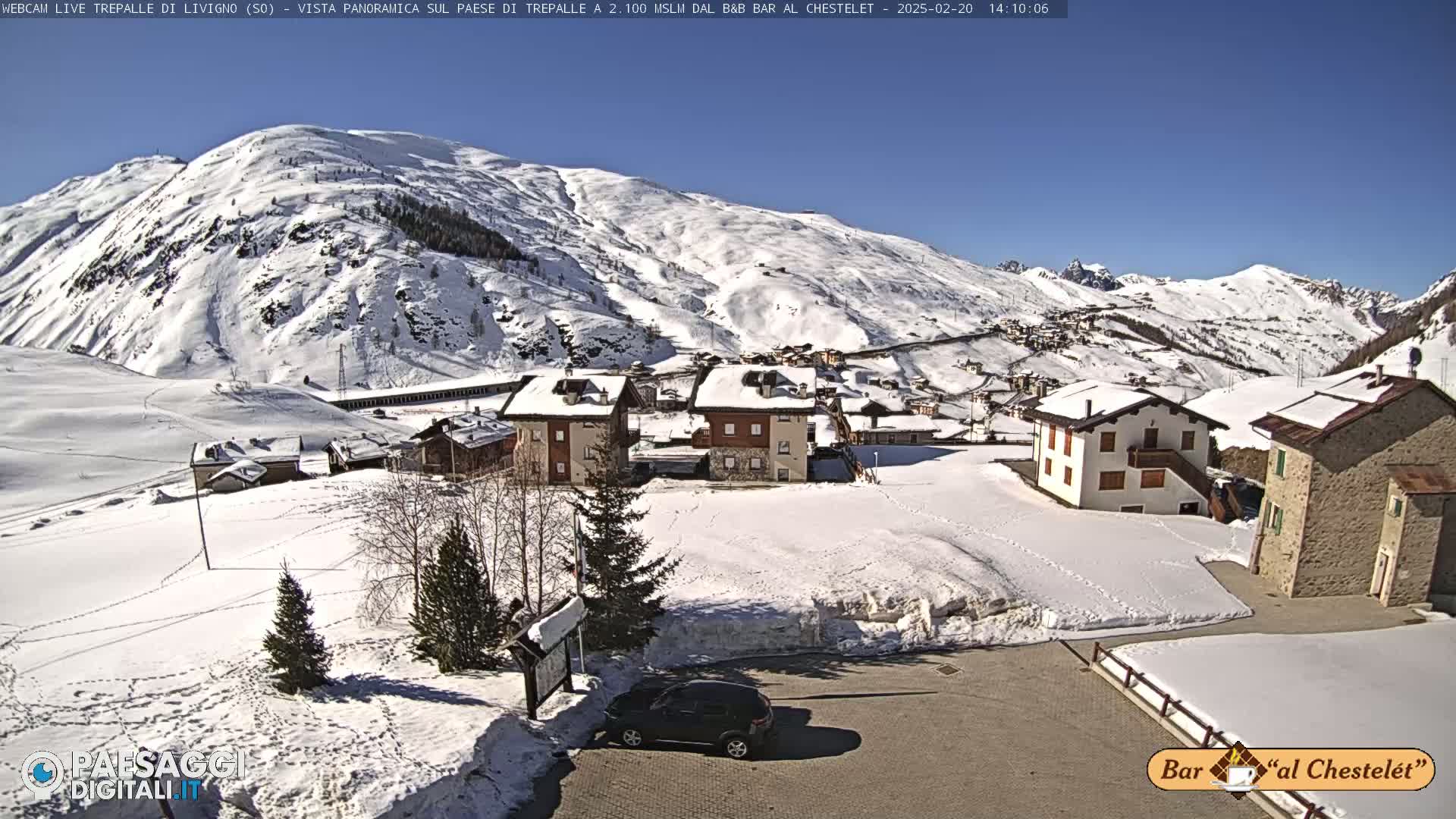 A snow-covered village nestled in a valley surrounded by snow-capped mountains under a clear blue sky.