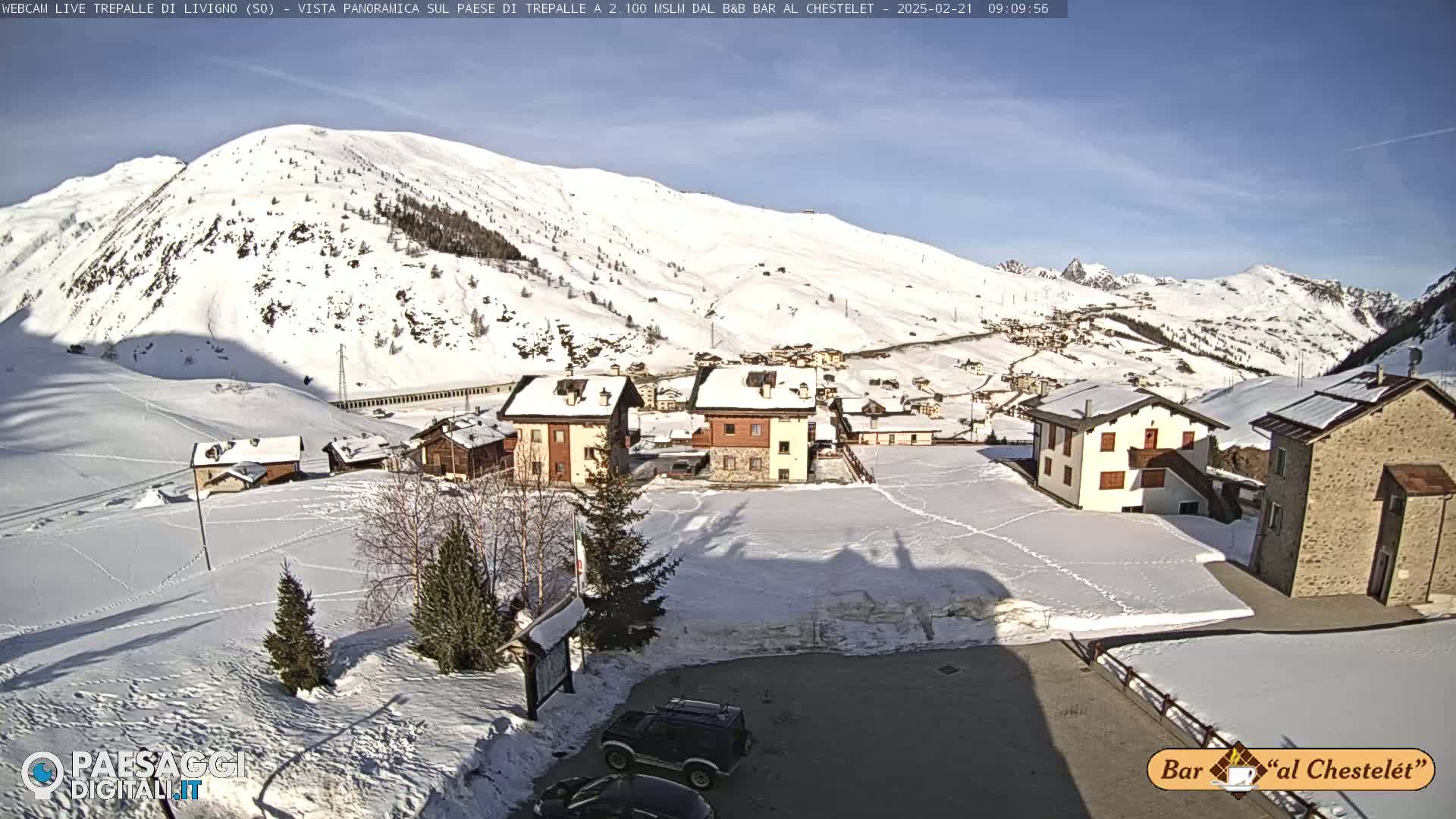A snow-covered village nestled in a valley beneath a sunny, snow-capped mountain.
