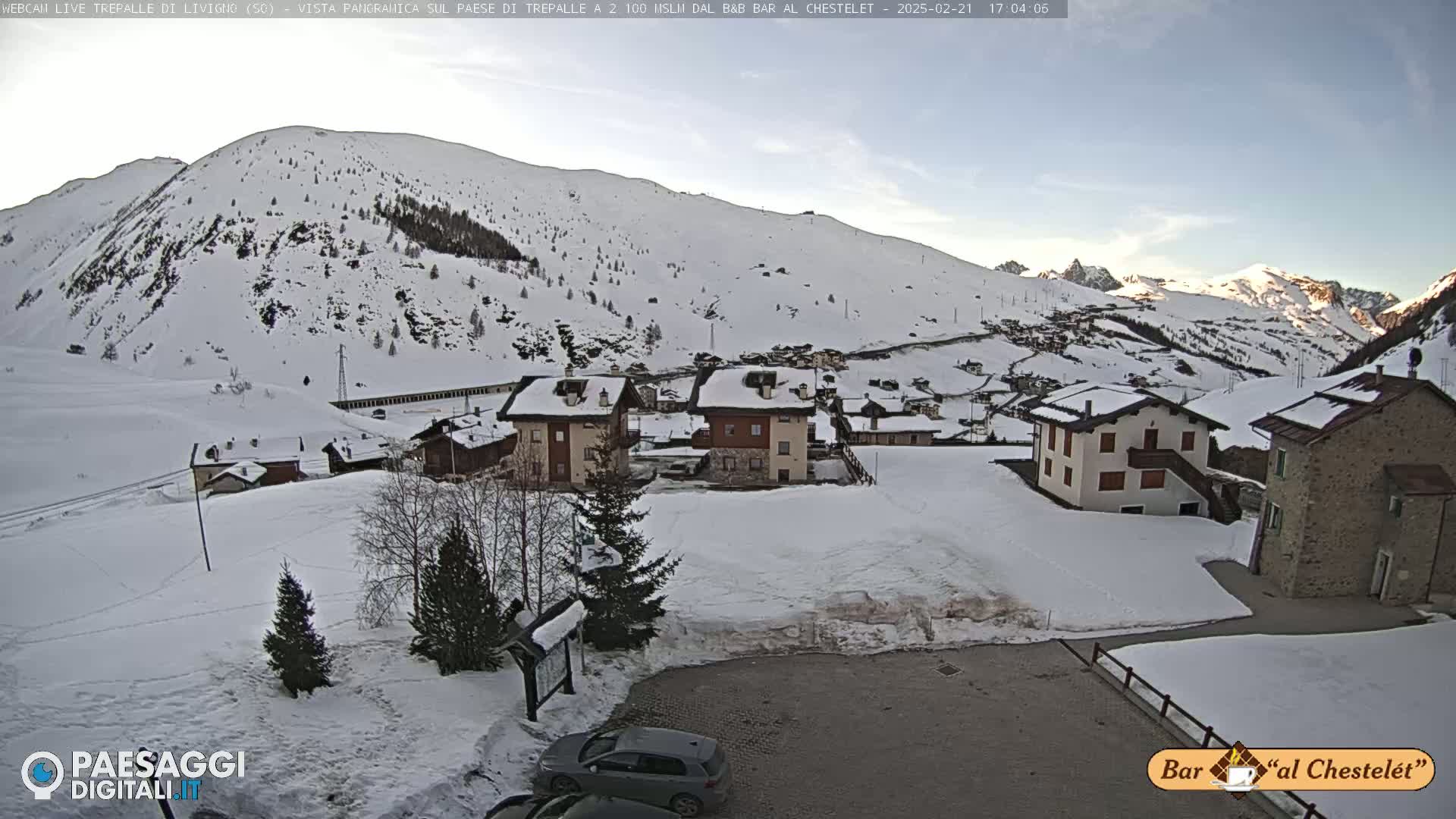 A snow-covered village nestled in a valley between snow-dusted mountains under a mostly clear sky.