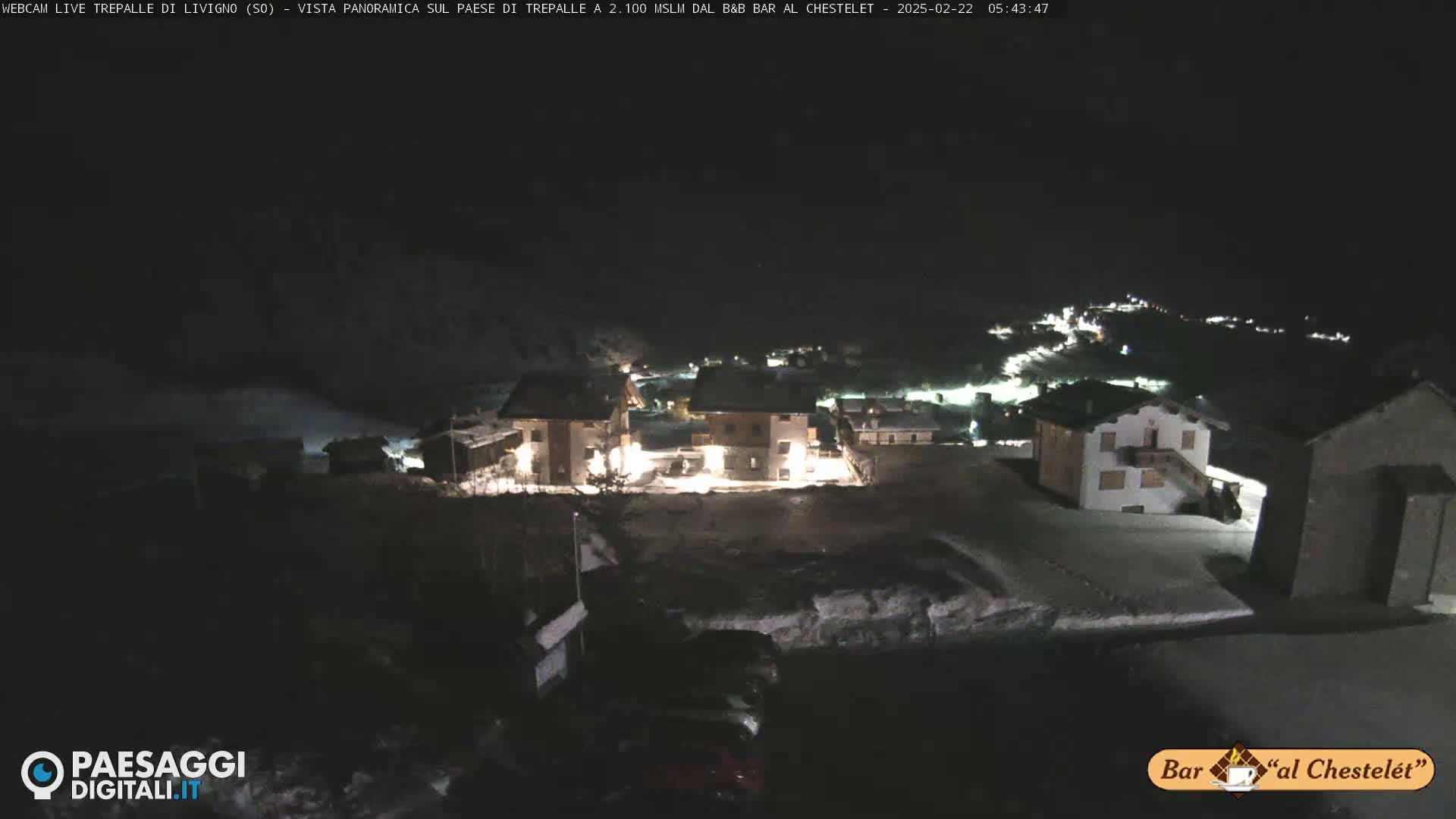 A nighttime, snow-covered village is illuminated by scattered lights under a dark sky.
