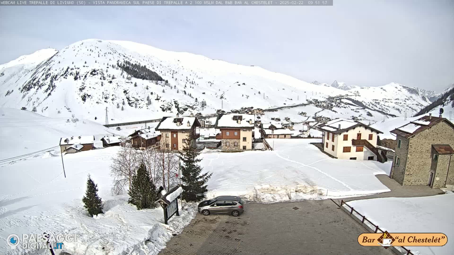 A snow-covered village nestled in a valley between snow-capped mountains under an overcast sky.