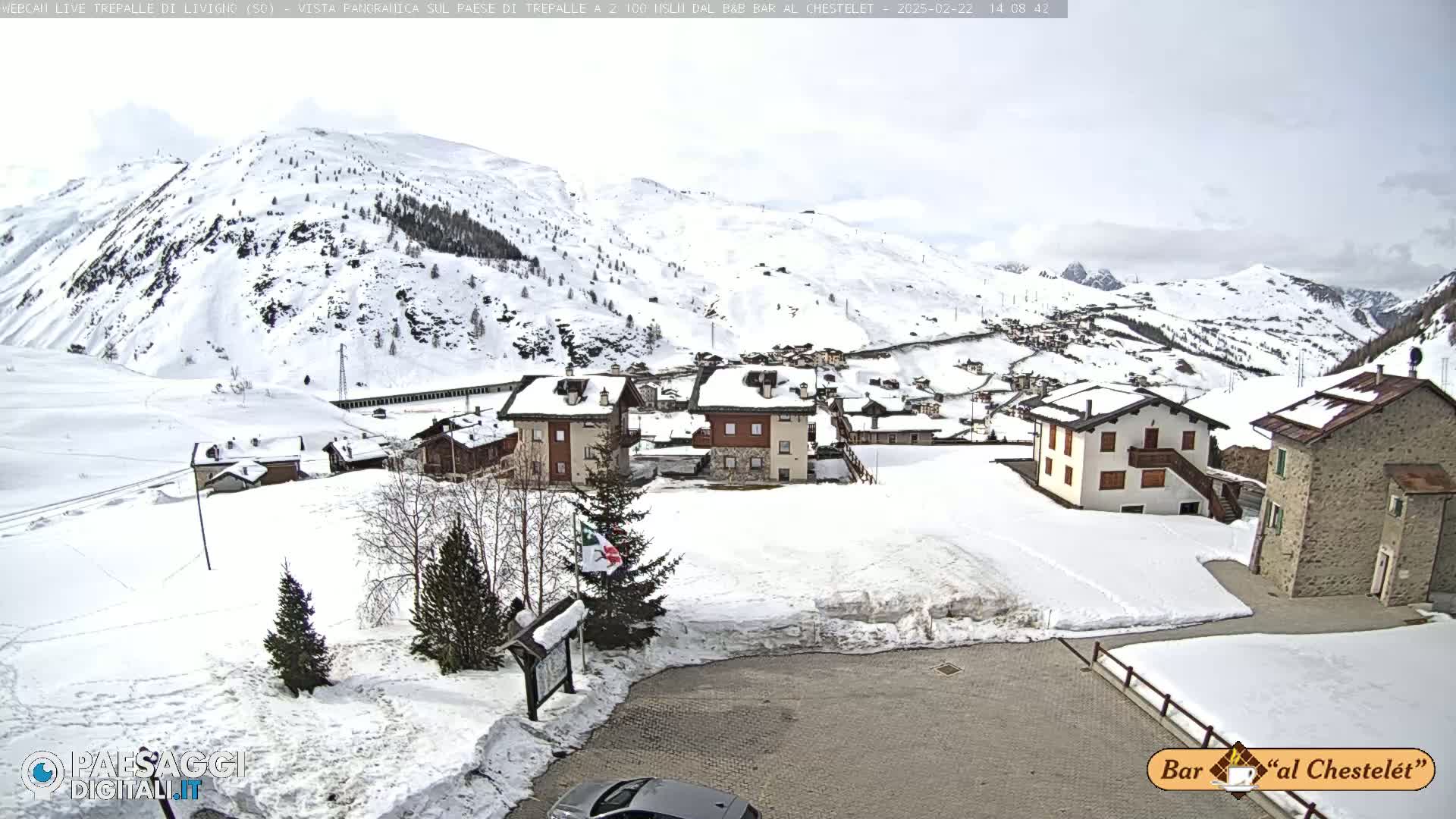 A snow-covered village nestled in a valley between snow-dusted mountains under an overcast sky.