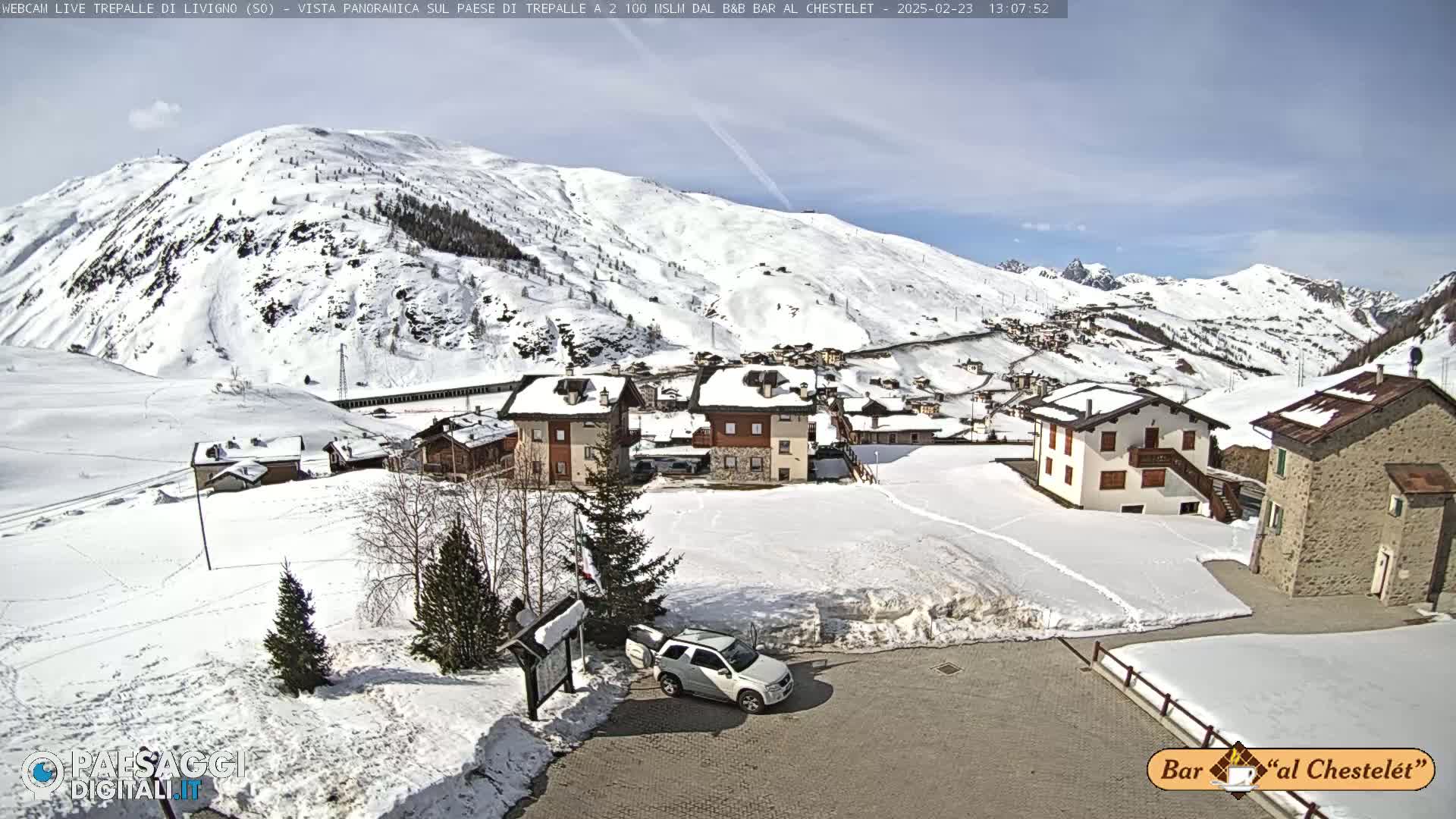A snow-covered village nestled in a valley surrounded by snow-capped mountains under a mostly clear sky.