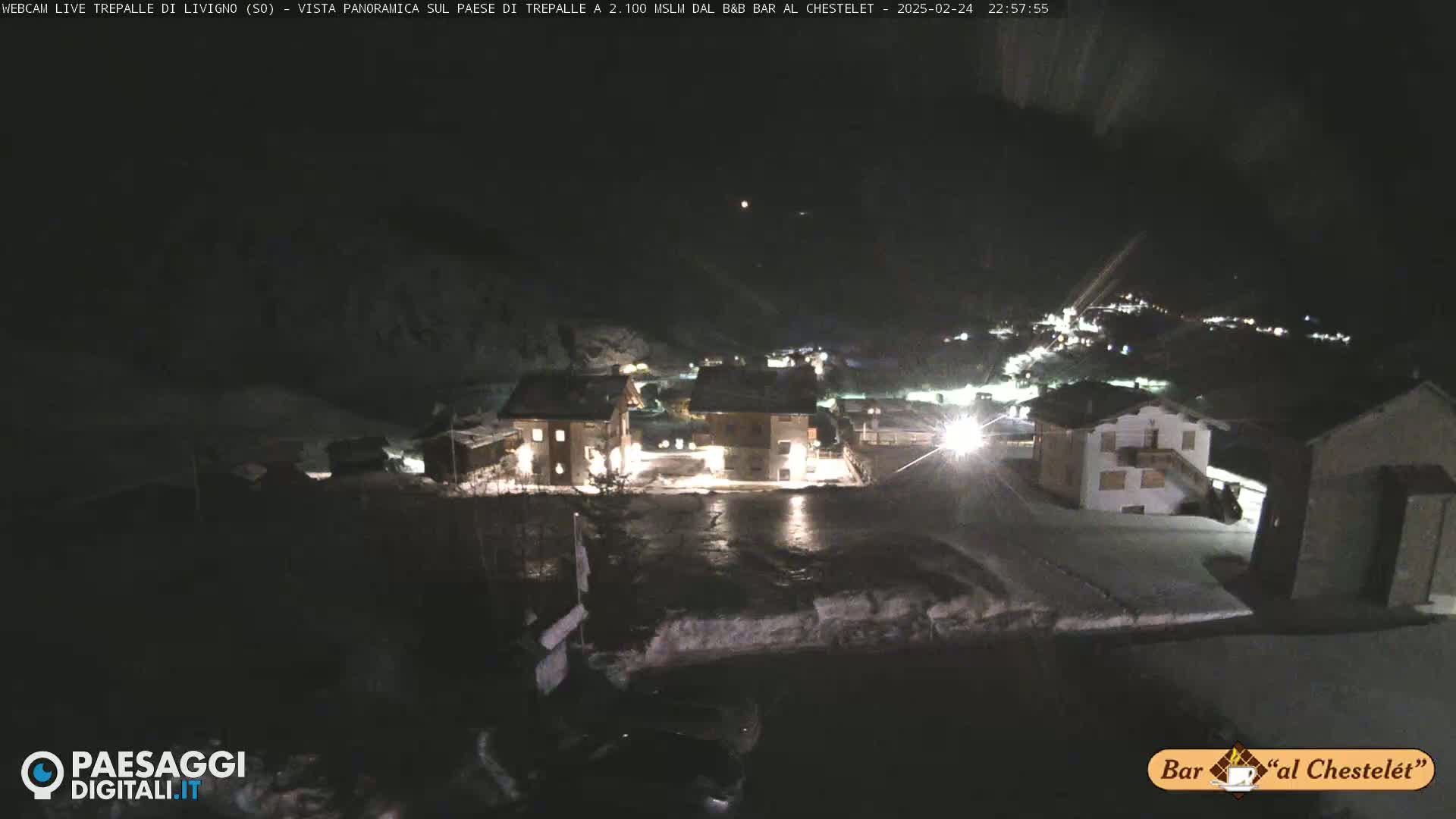 A nighttime view of a snow-covered village illuminated by artificial lights under a dark sky.