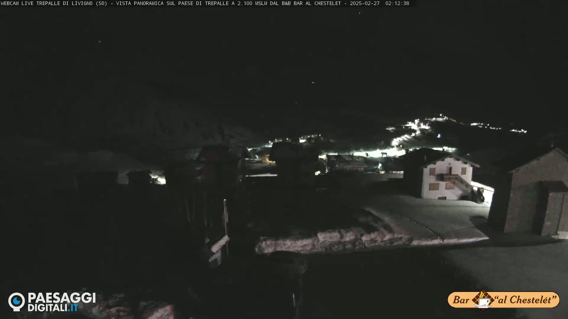 A nighttime, snow-covered village is seen from a high vantage point under a dark sky.