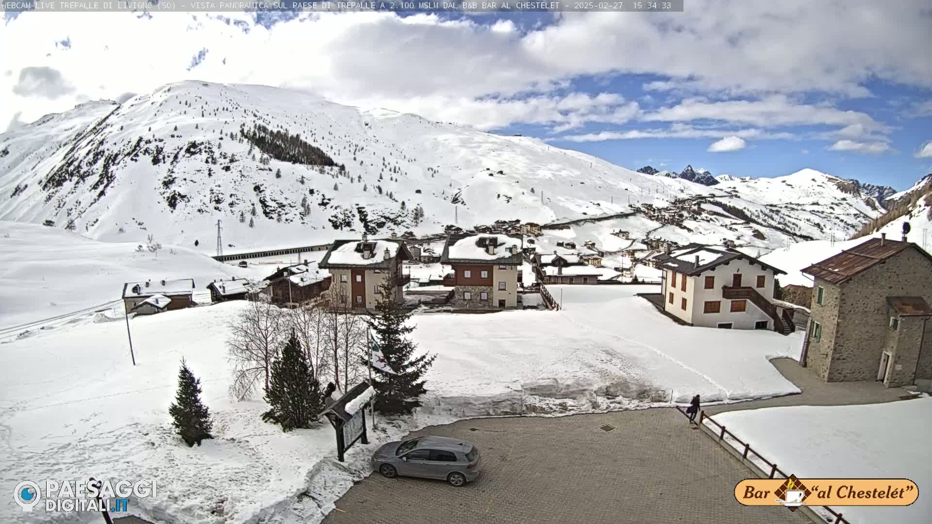 A snow-covered village nestled in a mountainous region under a partly cloudy sky.
