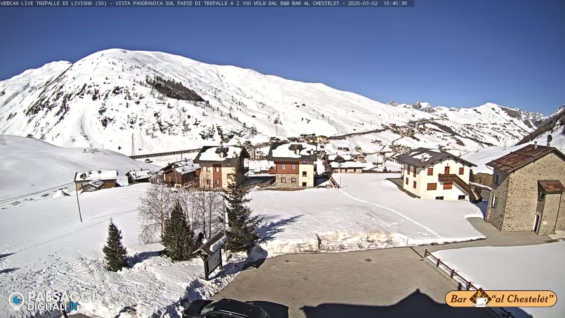 A snow-covered village nestled in a mountainous region under a clear, sunny sky.