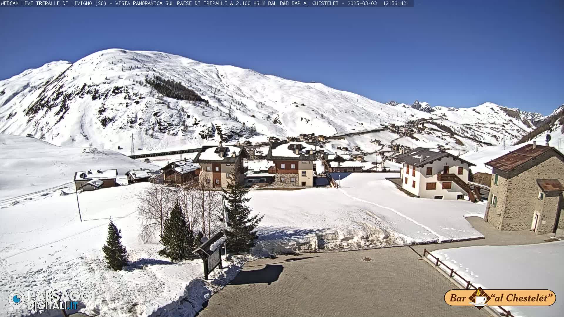 A snow-covered village nestled in a mountain valley under a clear blue sky.