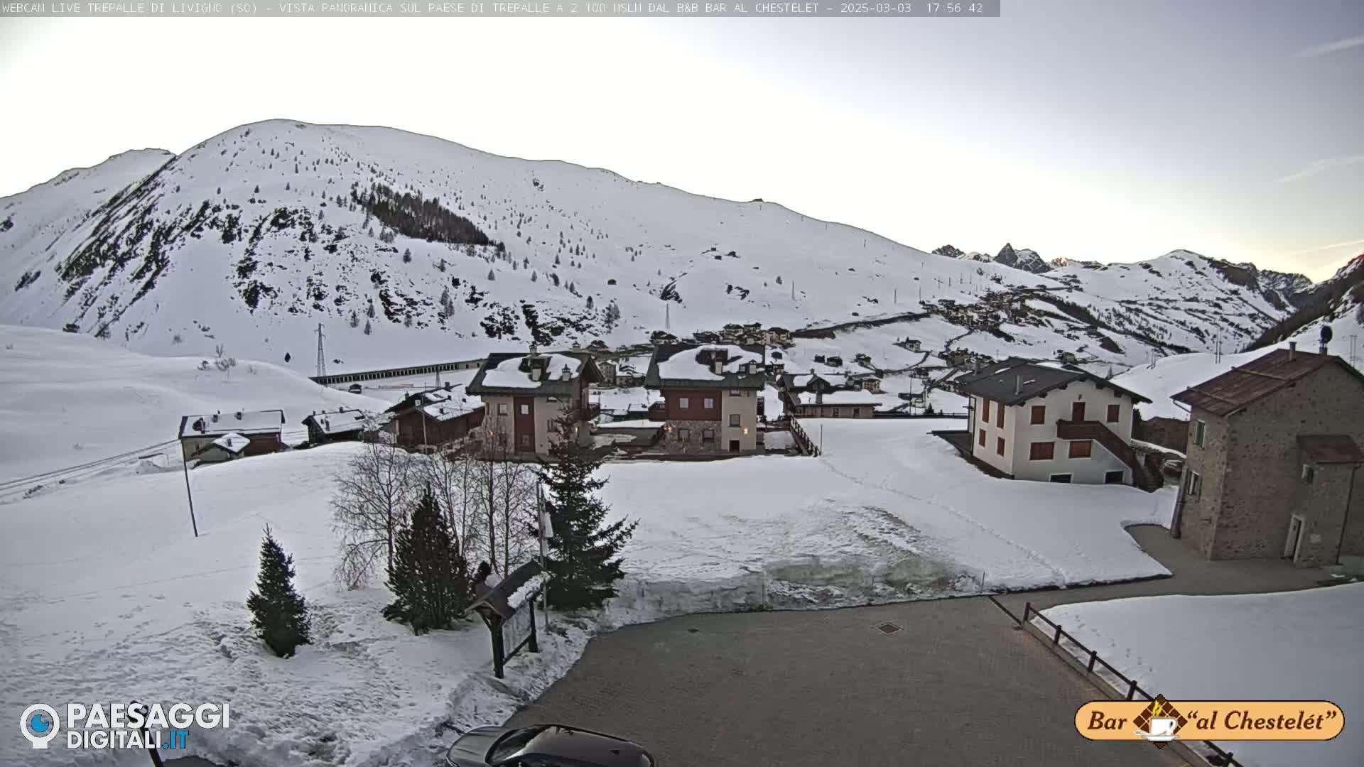 A snow-covered village nestled in a valley surrounded by snow-covered mountains under a clear, twilight sky.