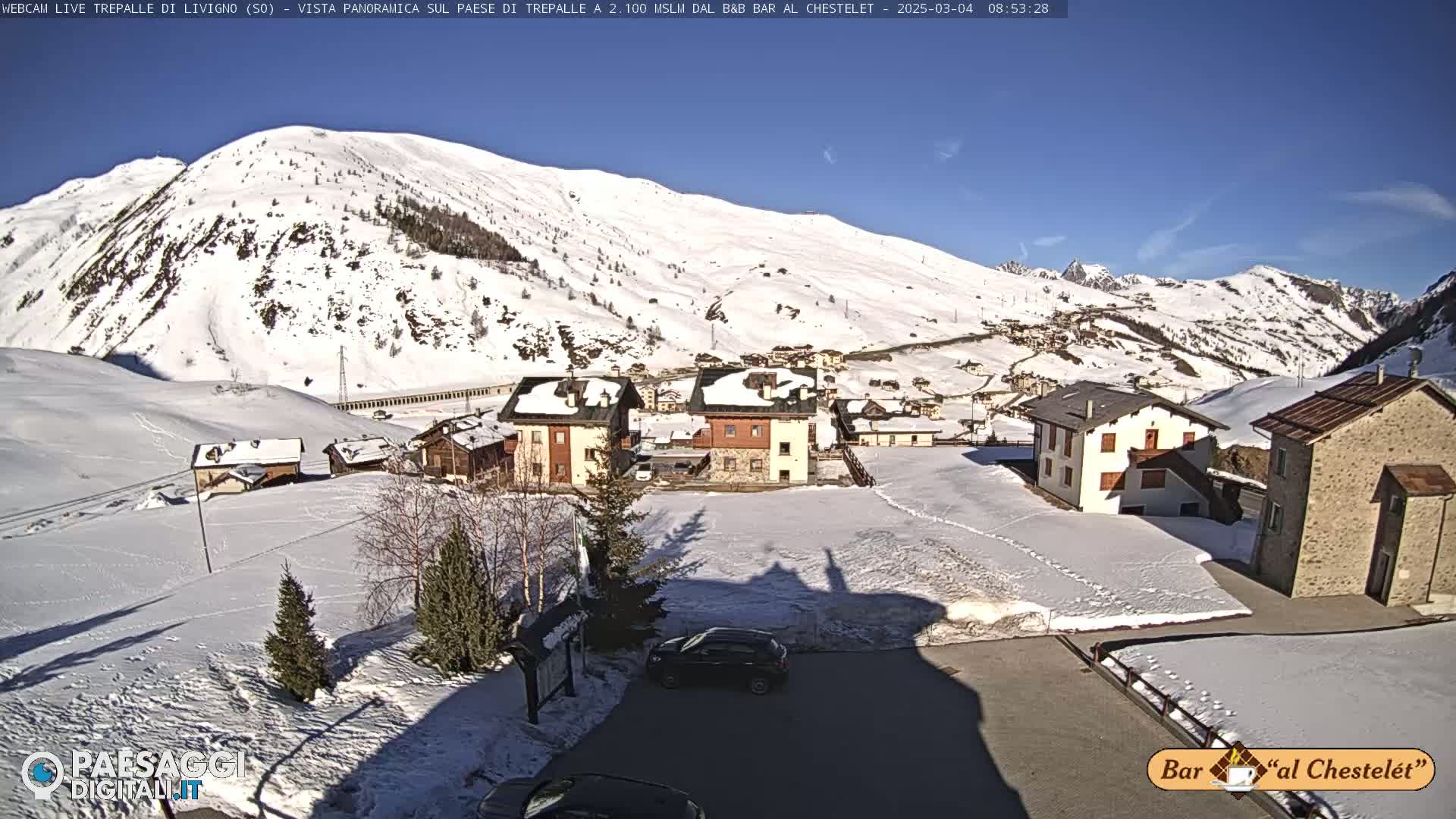 A snow-covered village nestled in a valley between snow-capped mountains under a clear blue sky.