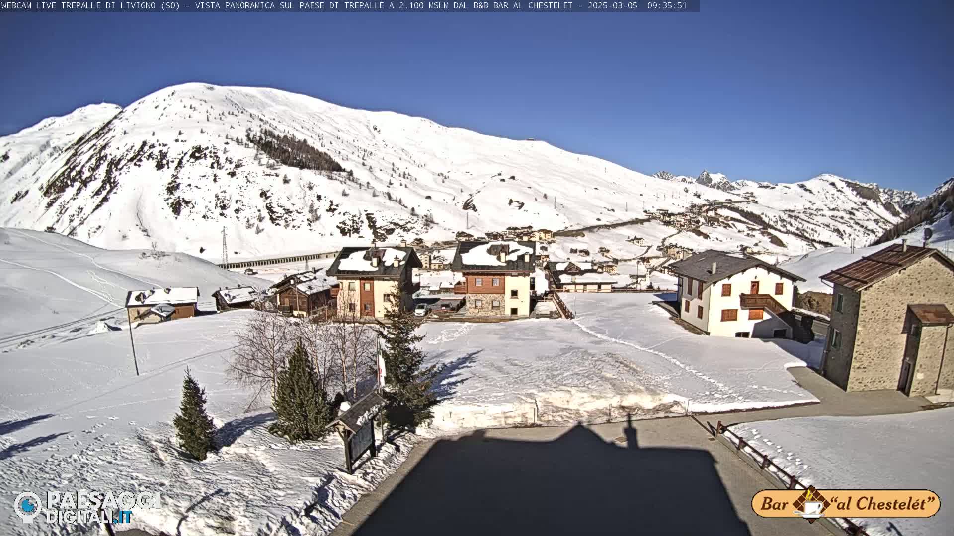 A snow-covered village nestled in a valley surrounded by snow-capped mountains under a clear blue sky.