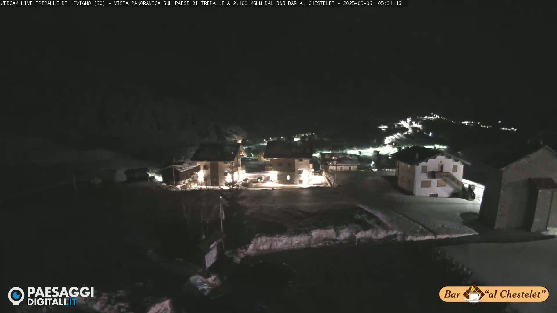 A nighttime, snow-covered village is illuminated by scattered lights under a dark sky.