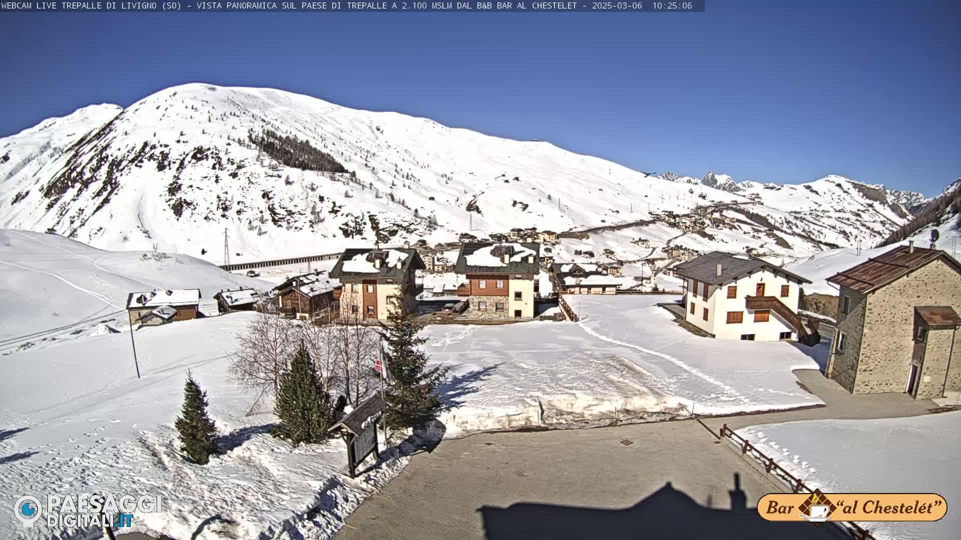 A snow-covered village nestled in a valley surrounded by snow-capped mountains under a clear, sunny sky.