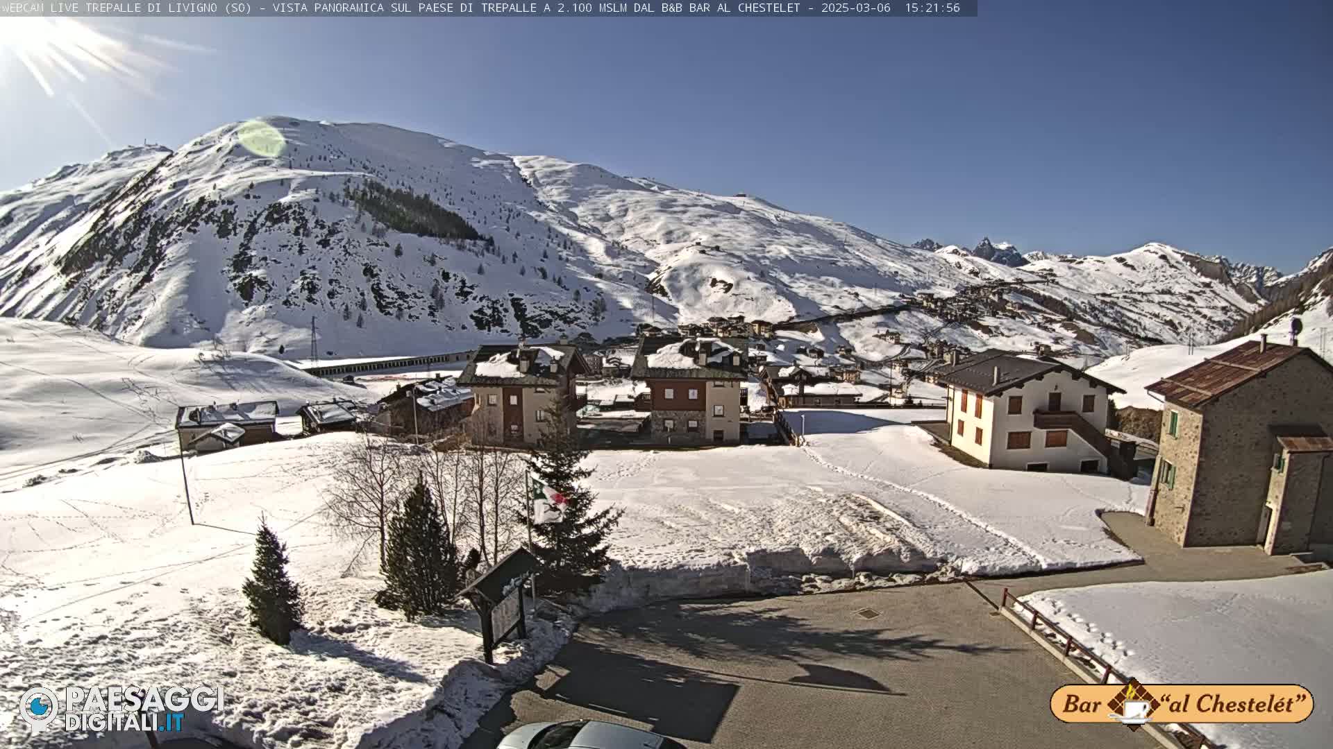 A sunny, snow-covered mountain village is nestled in a valley surrounded by snow-capped mountains.