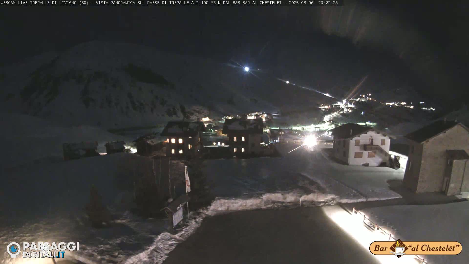 A snow-covered village is illuminated at night under a clear, dark sky.