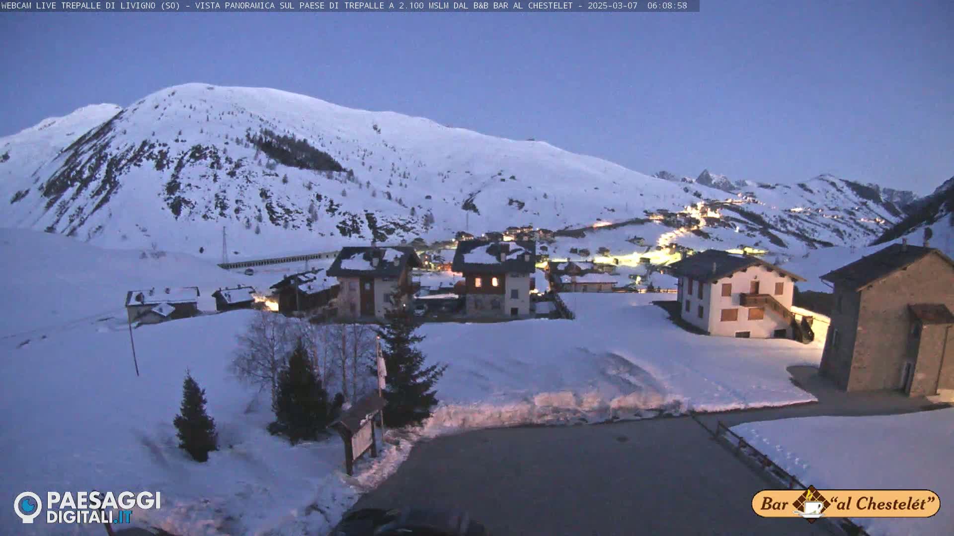 A snow-covered village nestled in a valley between snow-capped mountains under a twilight sky.