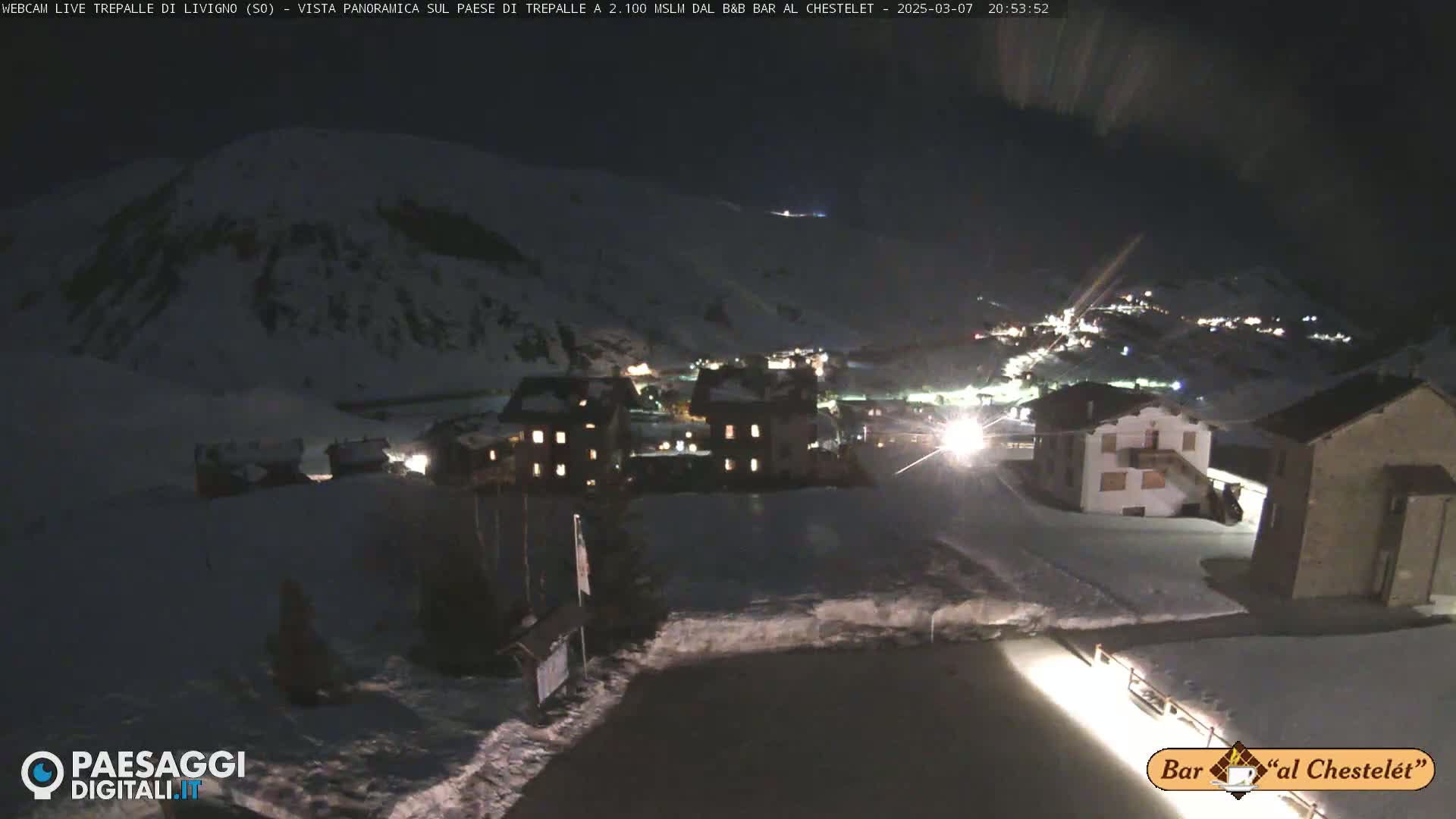 A nighttime view of a snow-covered village nestled in a mountainous area, illuminated by lights from buildings.