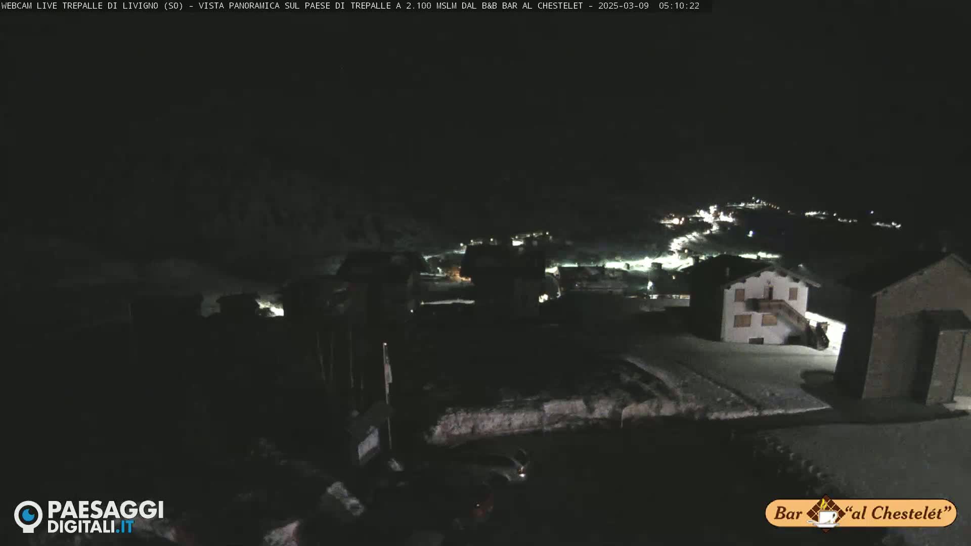 A nighttime, snow-covered village is illuminated by scattered lights, under a dark sky.