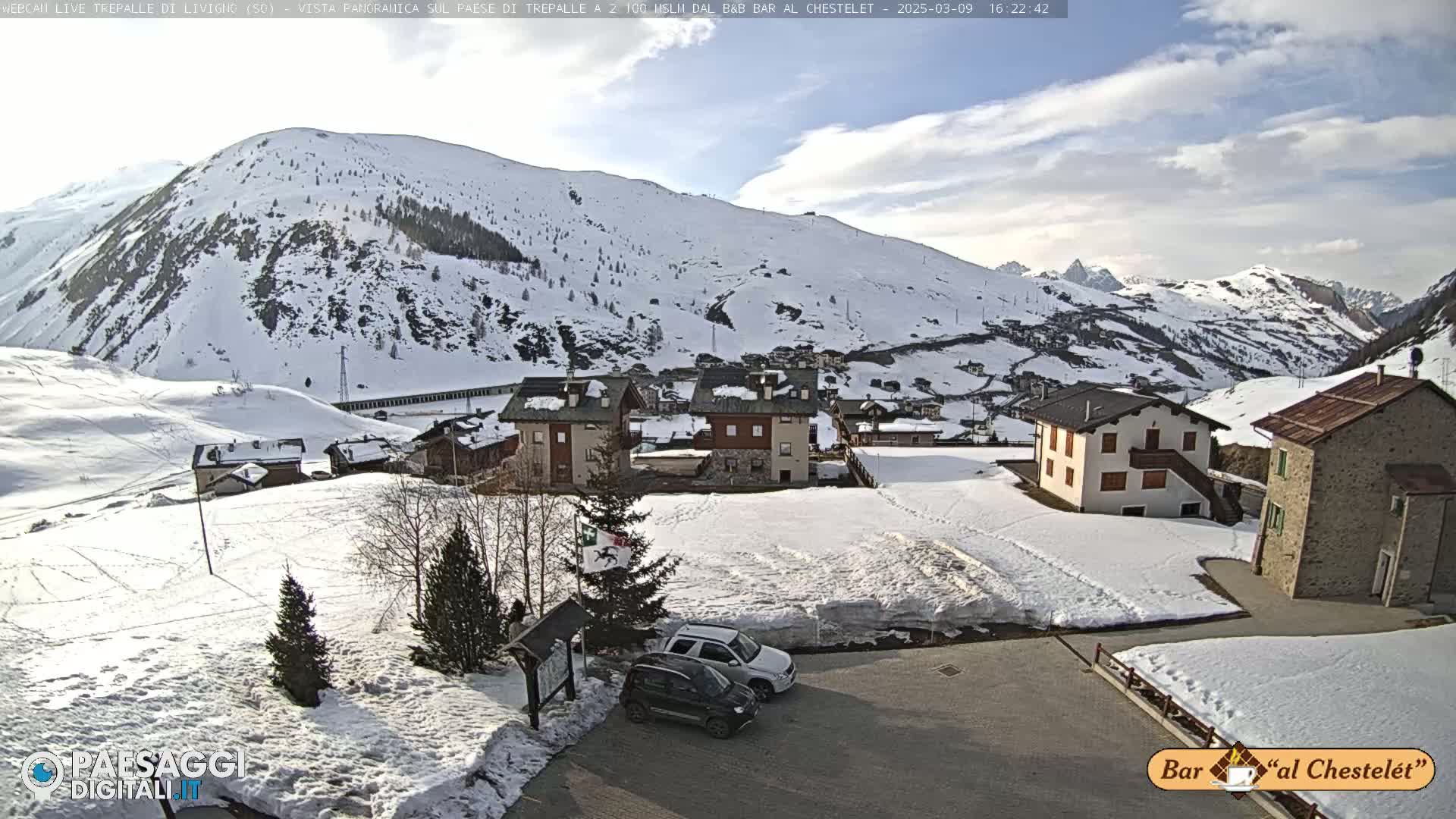 A snow-covered mountain village with several buildings is visible under a partly cloudy sky.
