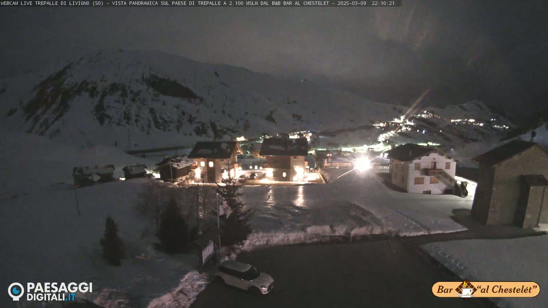 A nighttime view of a snow-covered village nestled in a mountainous region under a dark sky.