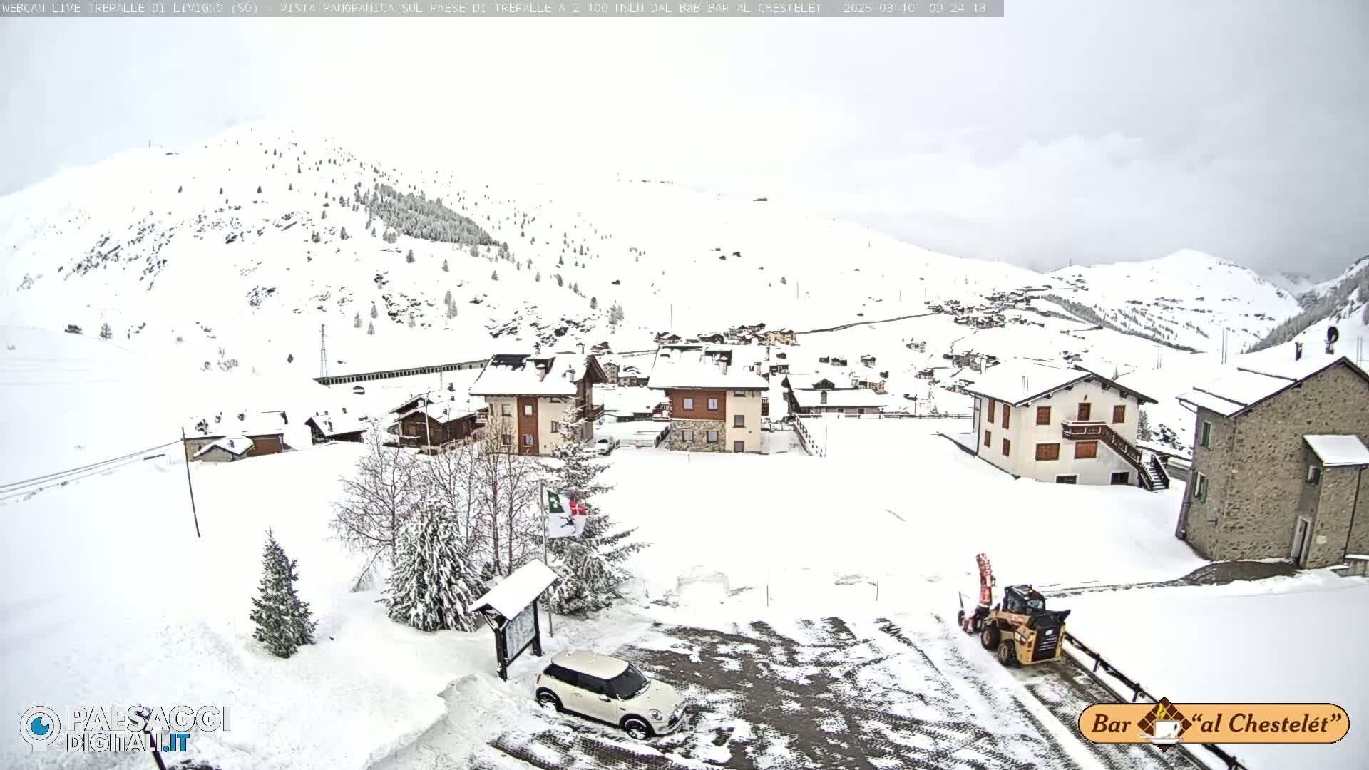 A snow-covered village nestled in a mountainous region, with a snowplow clearing a road.