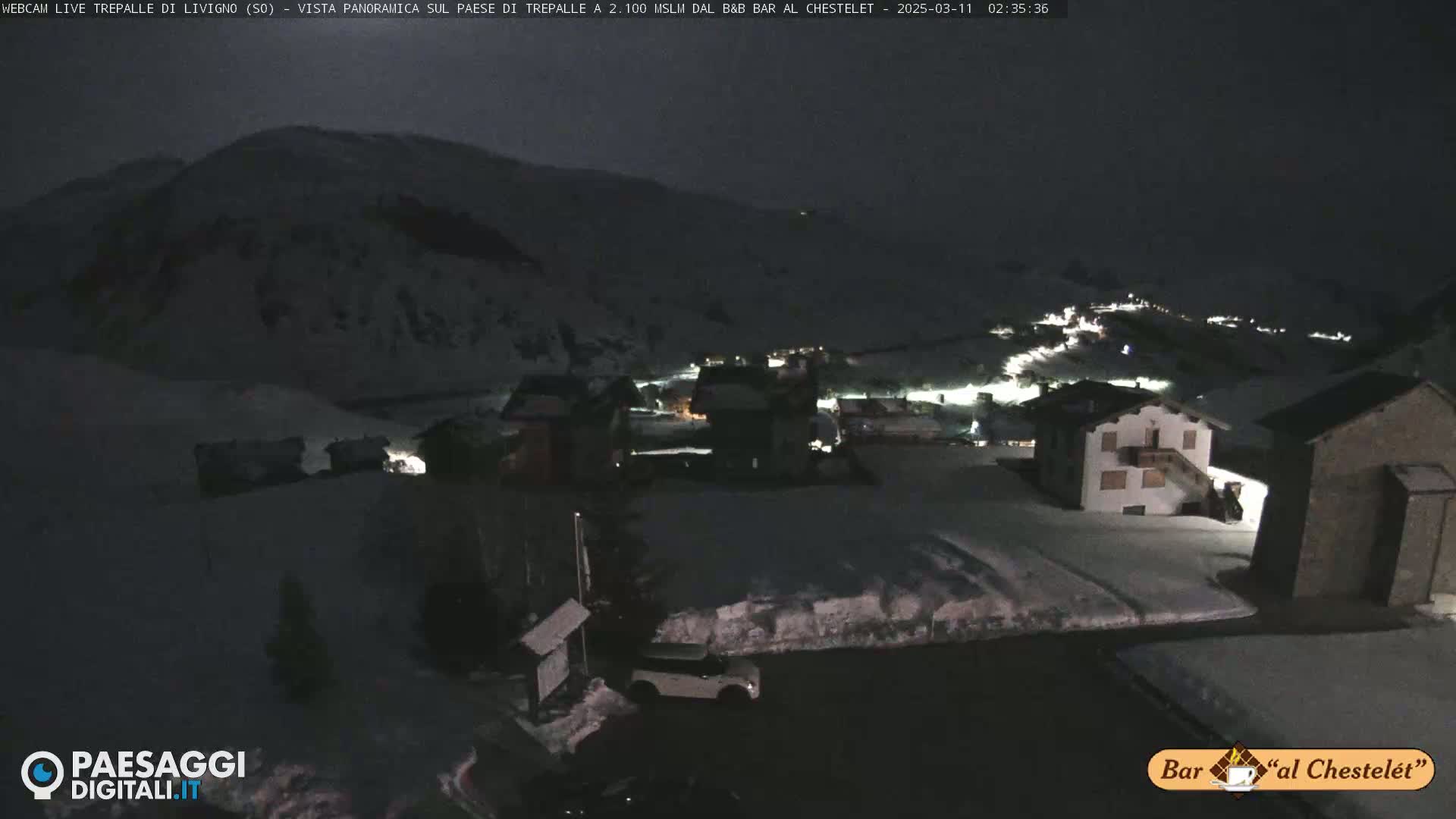 A nighttime, snow-covered village nestled in a mountain valley under a dark sky.