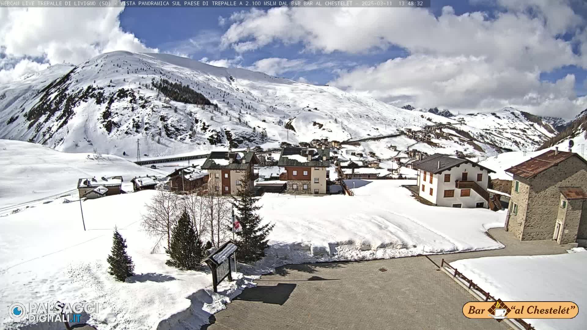 A snow-covered village nestled in a mountainous region under a partly cloudy sky.