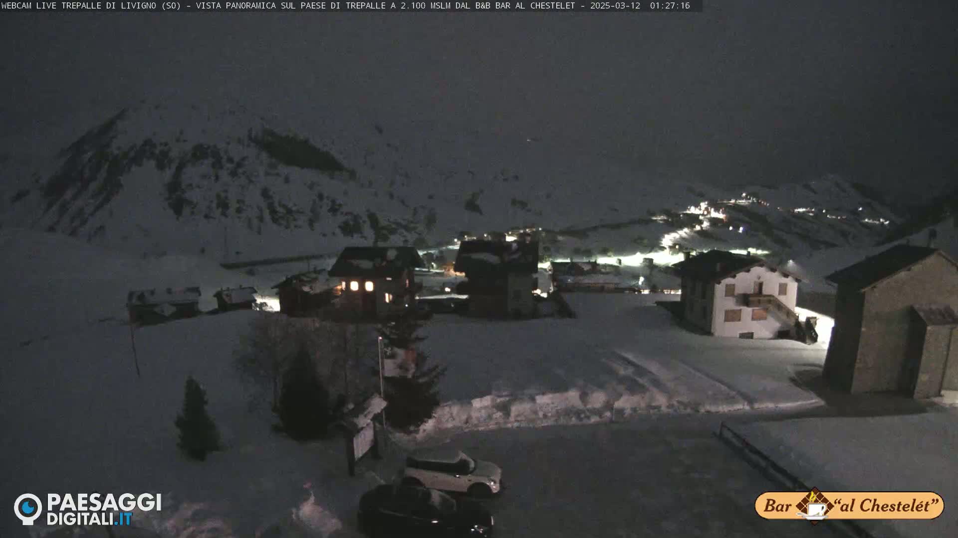 A snow-covered mountain village at night, illuminated by scattered lights, under a dark sky.