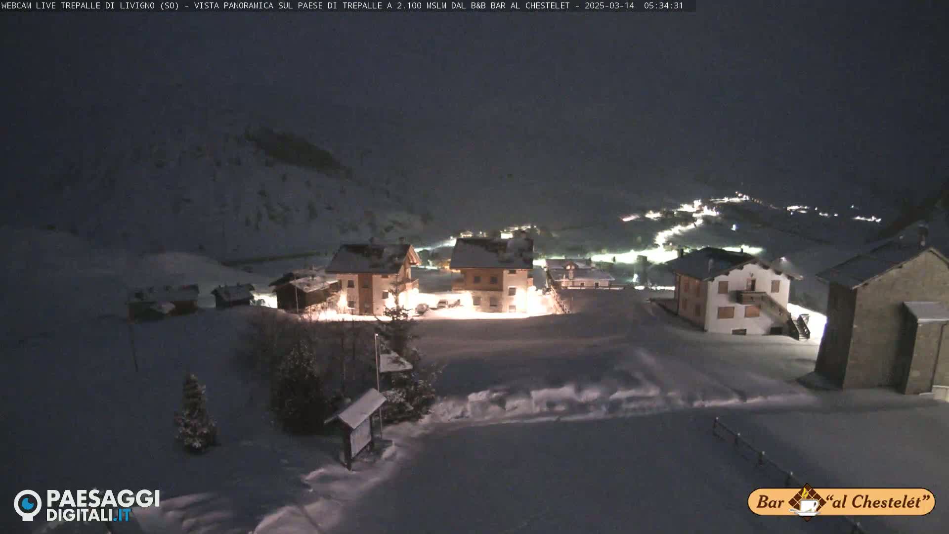 A snow-covered village is illuminated at night, with some buildings lit up.