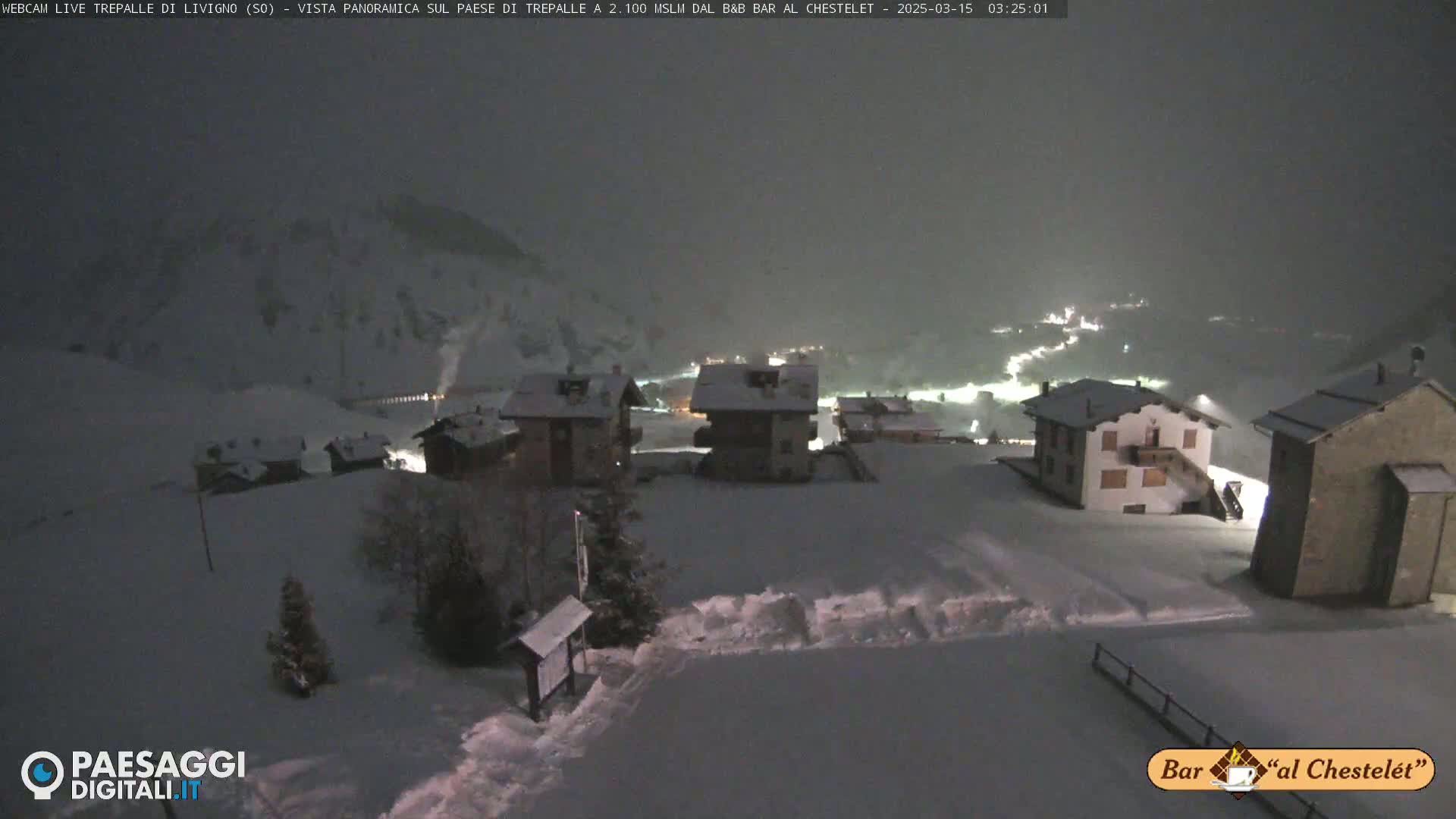 A snow-covered village at night, illuminated by scattered lights, under a dark, cloudy sky.