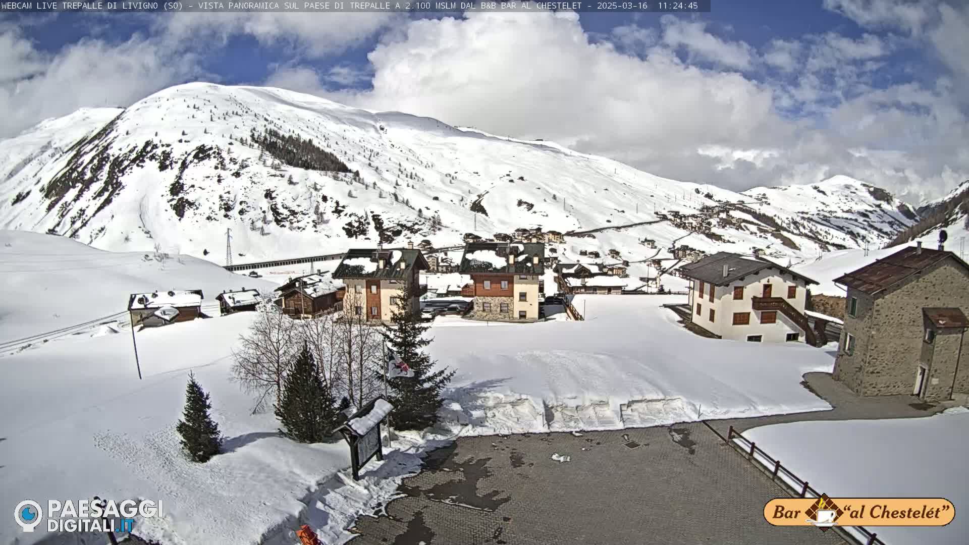 A snow-covered village nestled in a mountain valley under a partly cloudy sky.