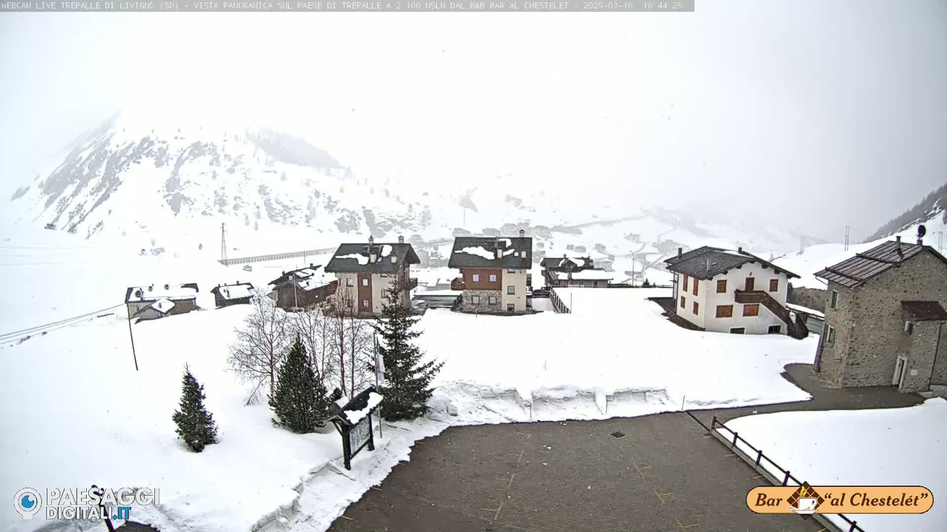 A snow-covered village nestled in a mountainous region is seen under hazy, snowy weather conditions.