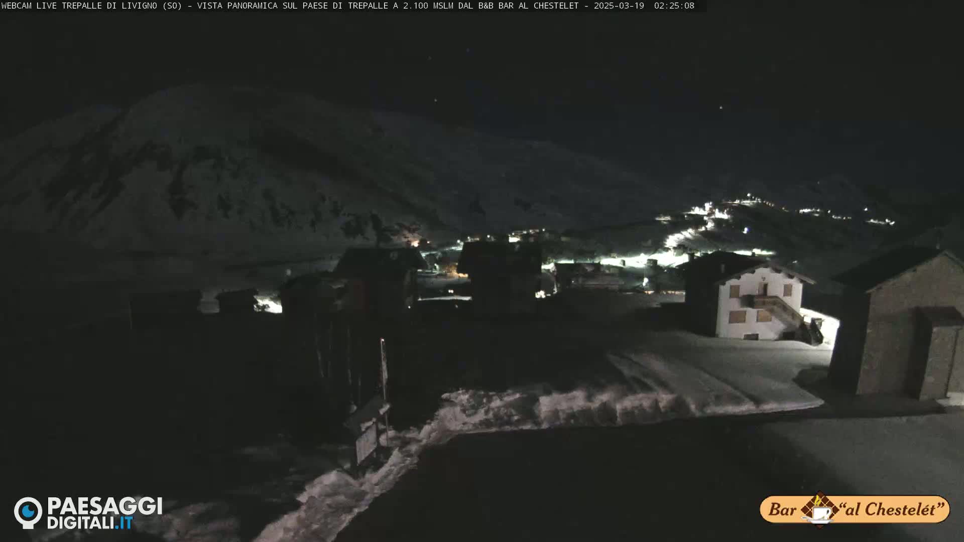 A nighttime, snow-covered village is nestled in a valley under a dark sky.