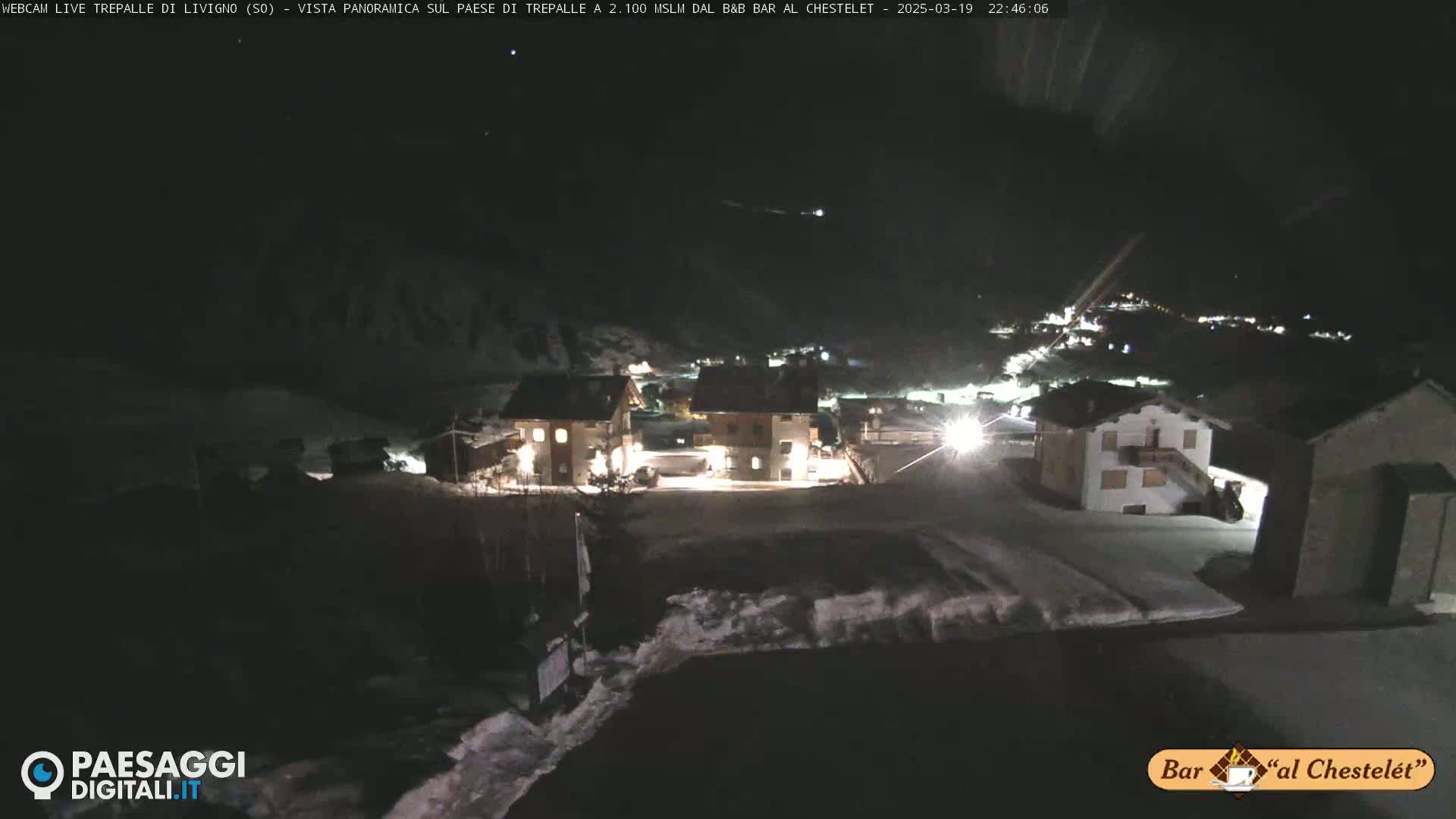 A nighttime, snow-covered village scene is illuminated by building lights under a dark, clear sky.