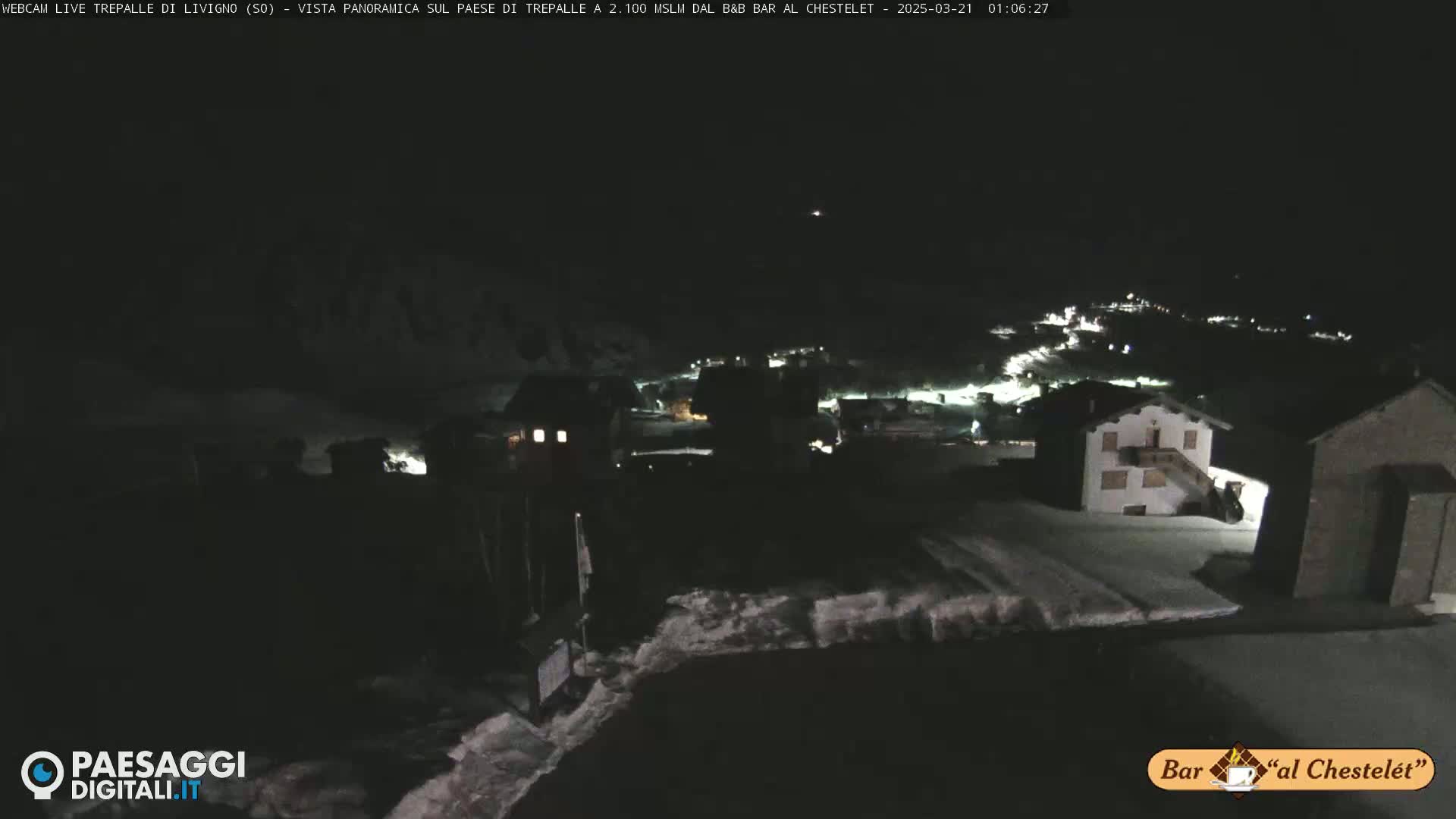 A nighttime, snow-covered village is illuminated by scattered lights under a dark sky.