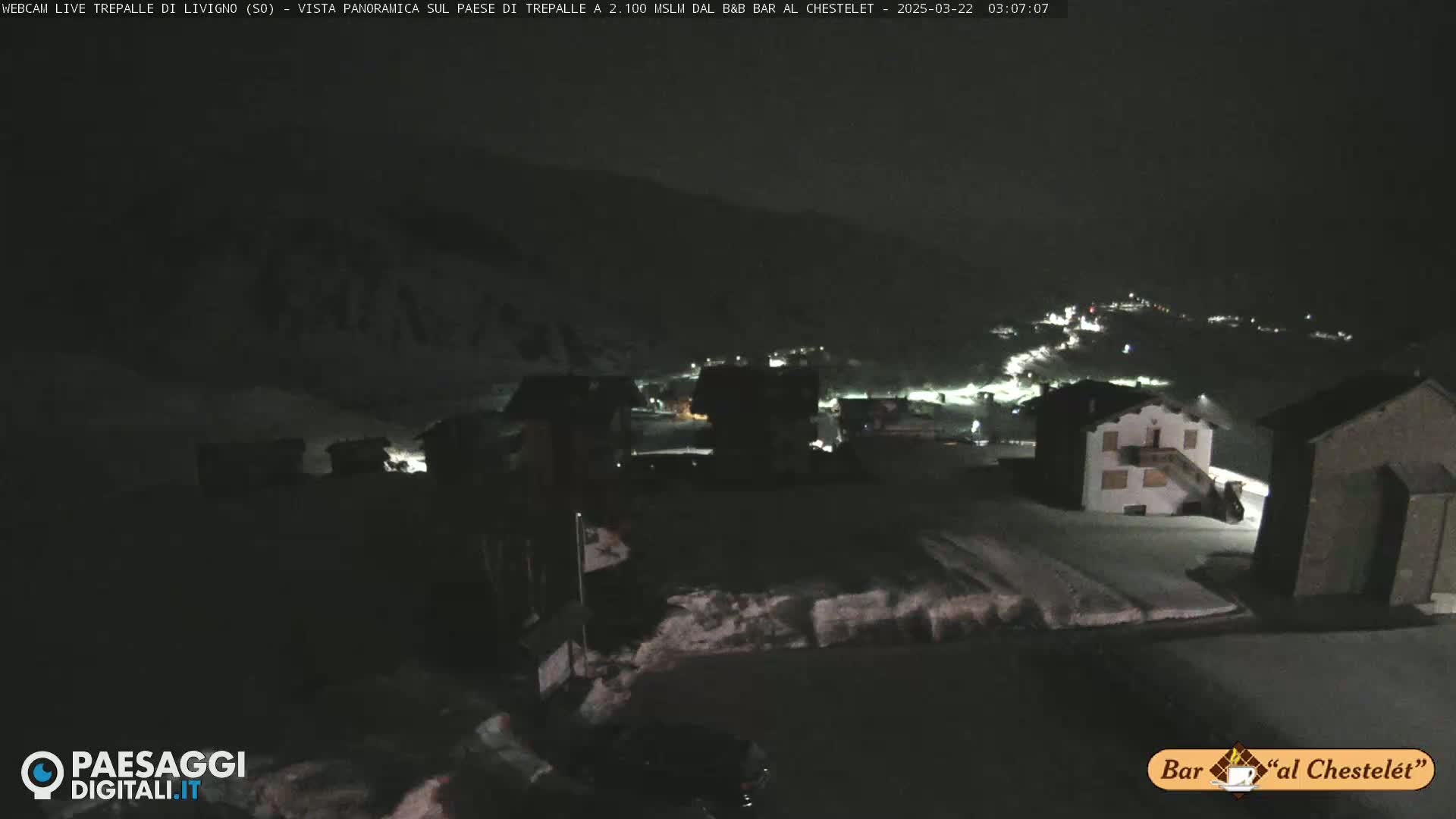 A nighttime, snow-covered village is illuminated by scattered lights under a dark sky.