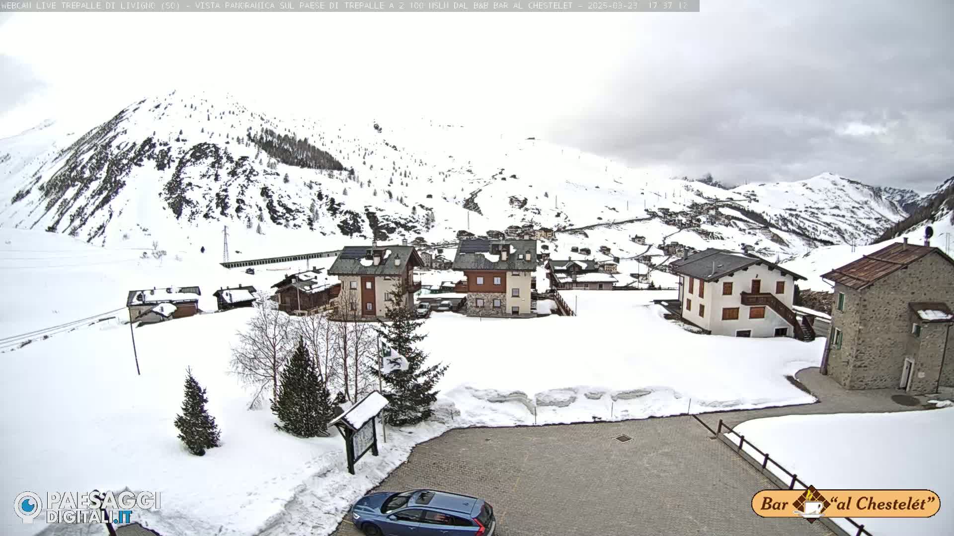 A snow-covered village nestled in a valley amongst snow-capped mountains under an overcast sky.