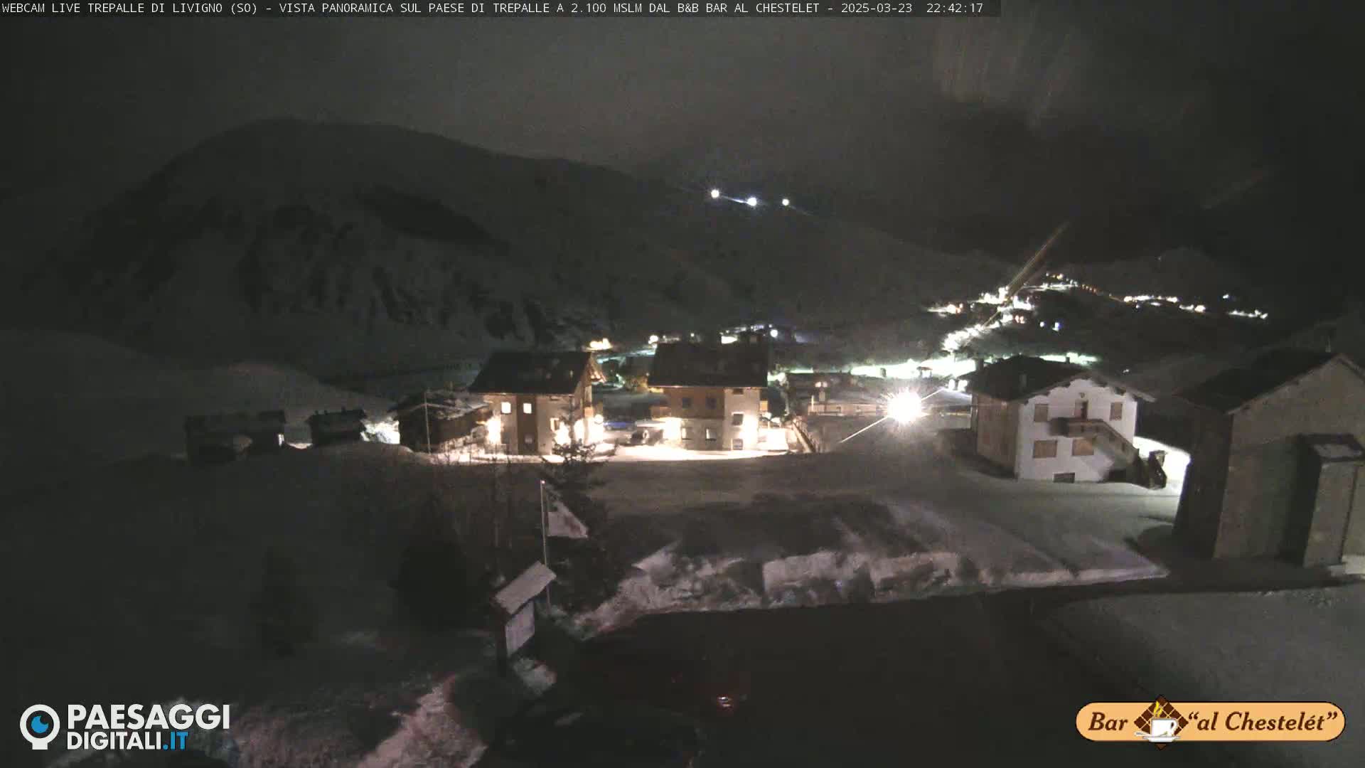 A nighttime, snow-covered village scene with several illuminated buildings nestled against a dark mountainside.