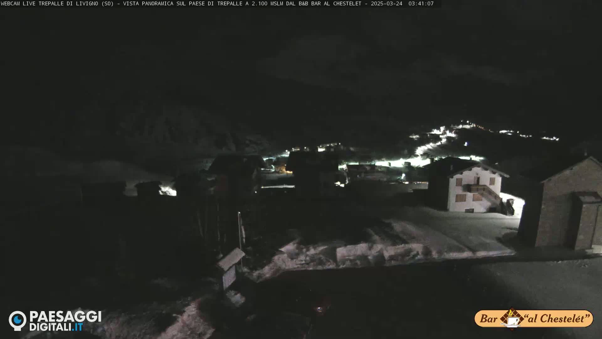 A nighttime, snow-covered village is illuminated by scattered lights under a dark sky.