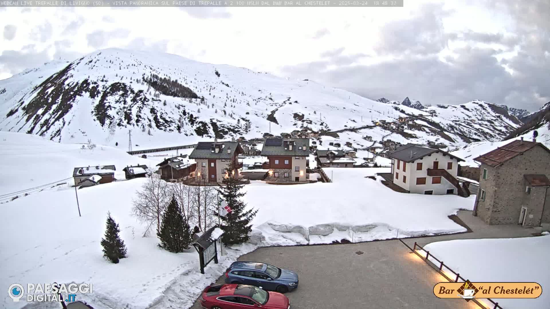 A snow-covered village nestled in a mountainous valley under a cloudy sky.